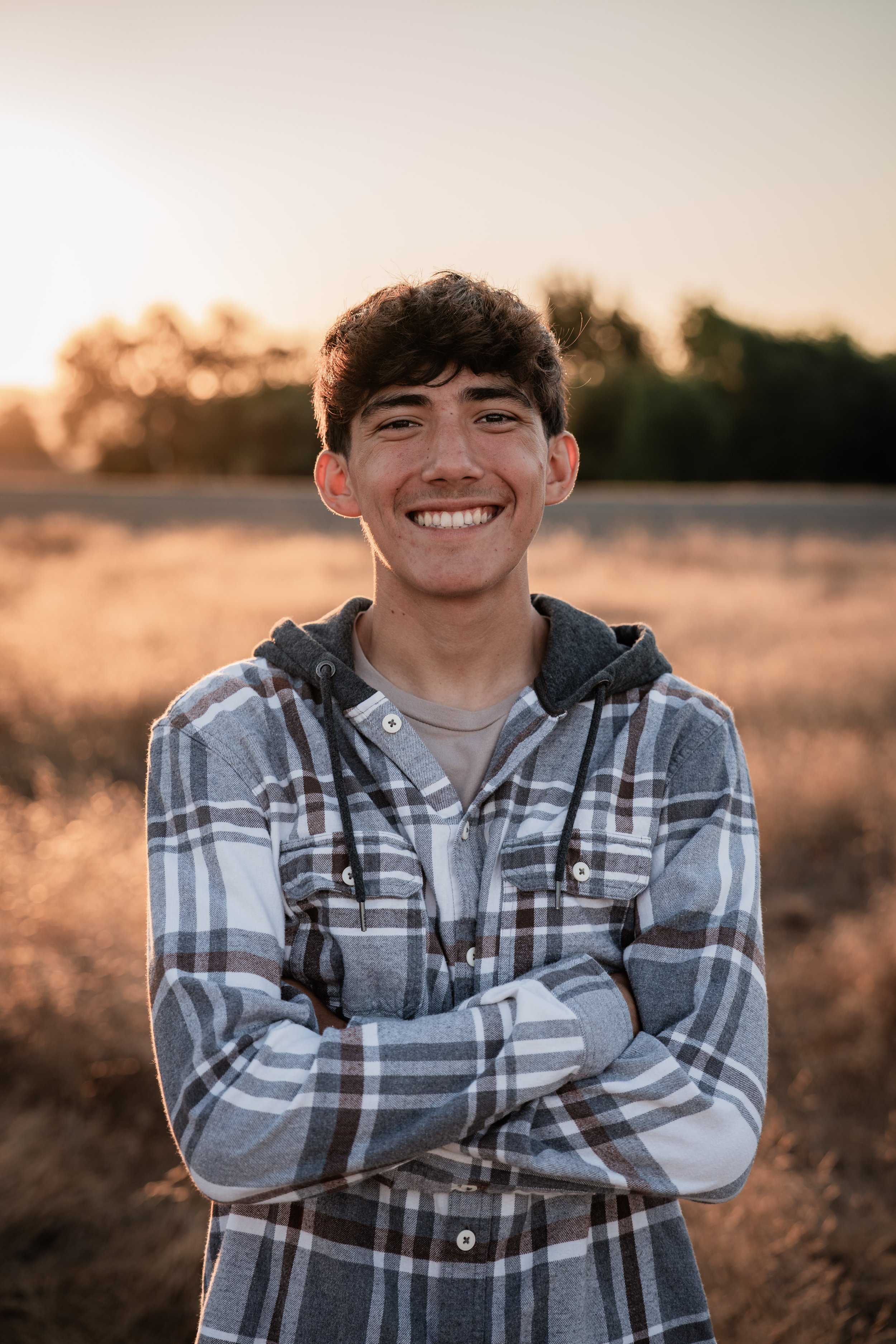 High school senior posing for a photo with his arms crossed in a plaid sweatshirt. Photo taken in Newman, CA by Mikaela Tosta Photography