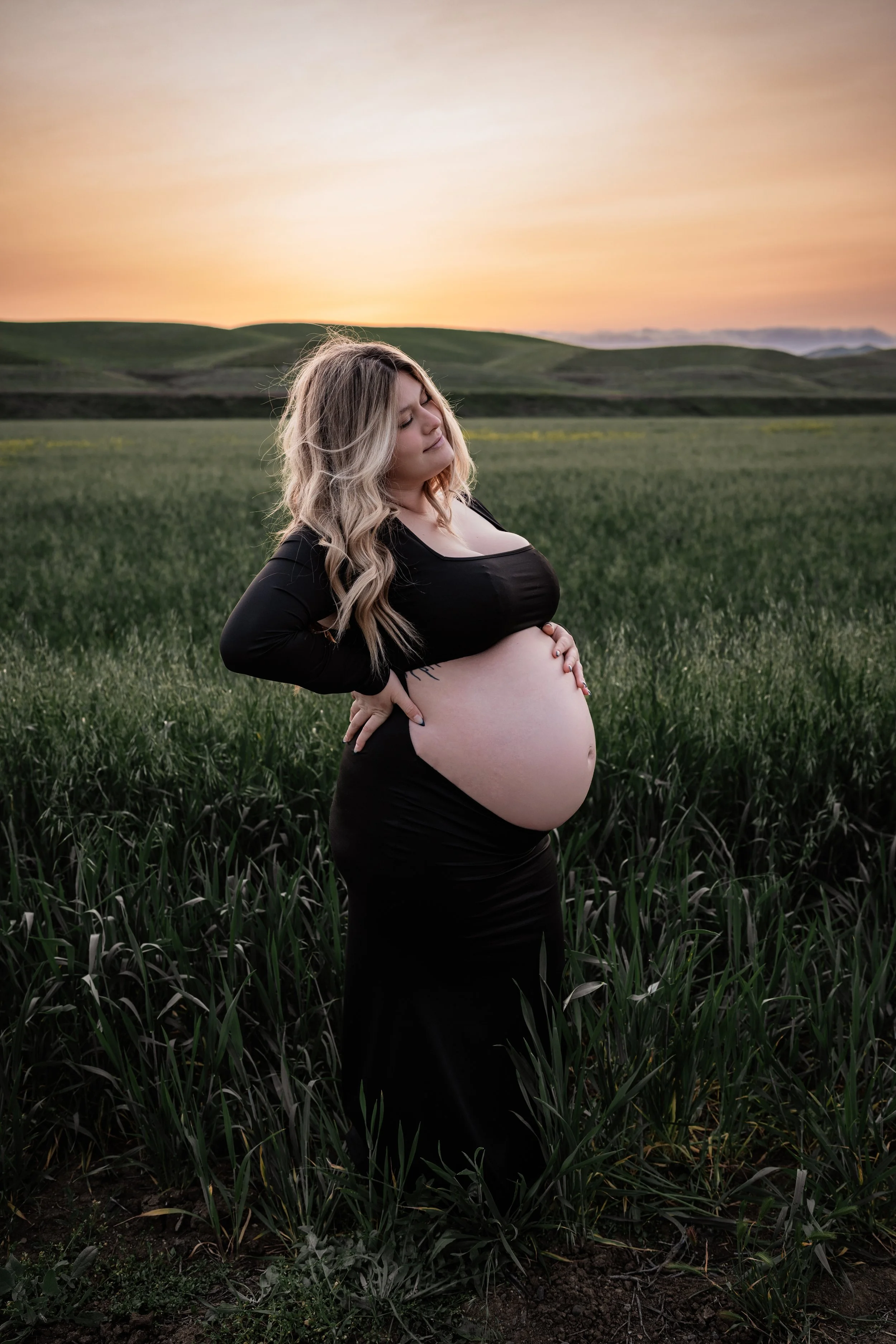 Pregnant mom holding her belly at sunset in an open field. Photo taken in Patterson, CA by Mikaela Tosta Photography.