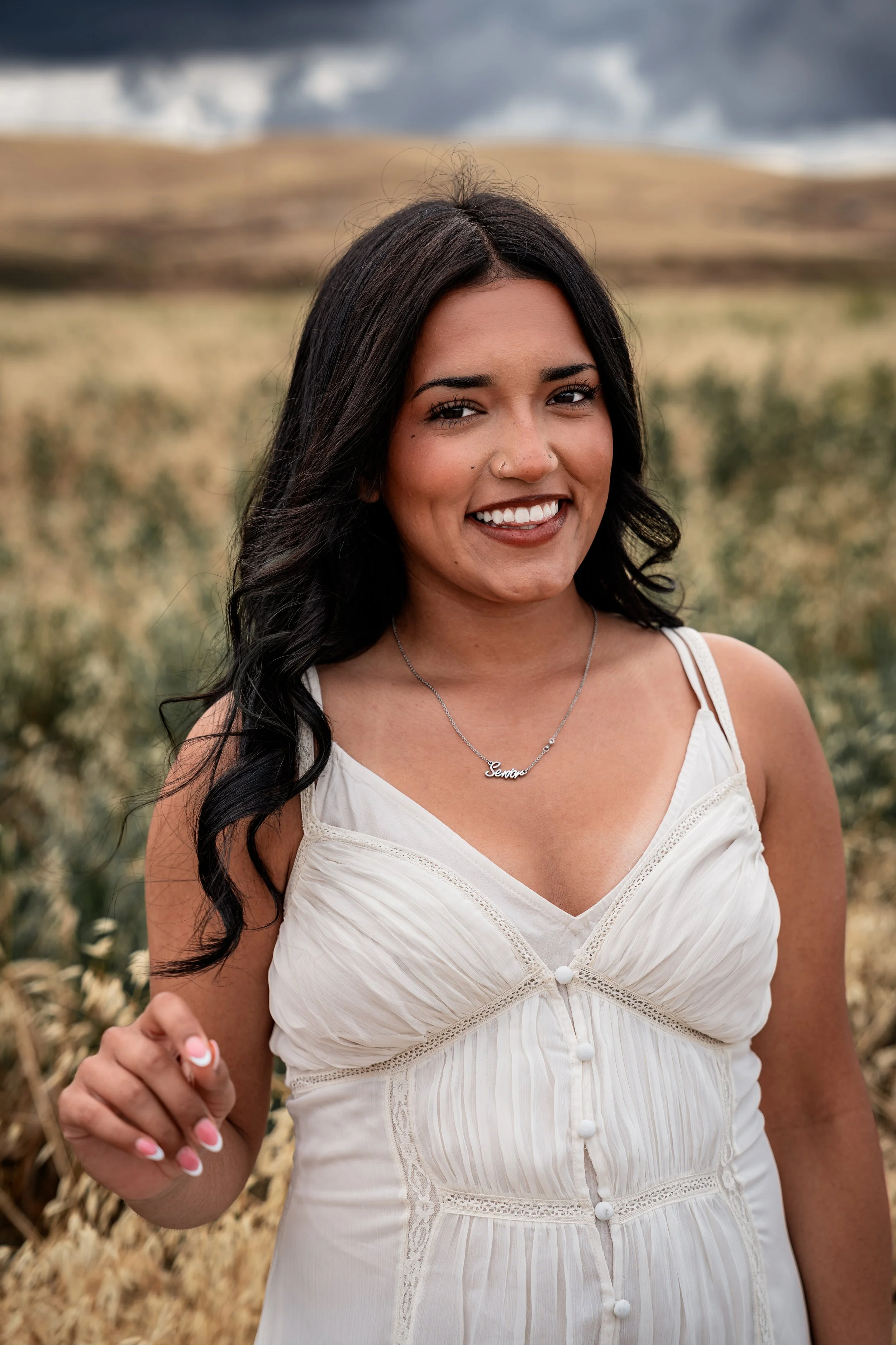 High school senior posing in a white dress while playing with her hair in an open field. Photo taken in Patterson, CA by Mikaela Tosta Photography