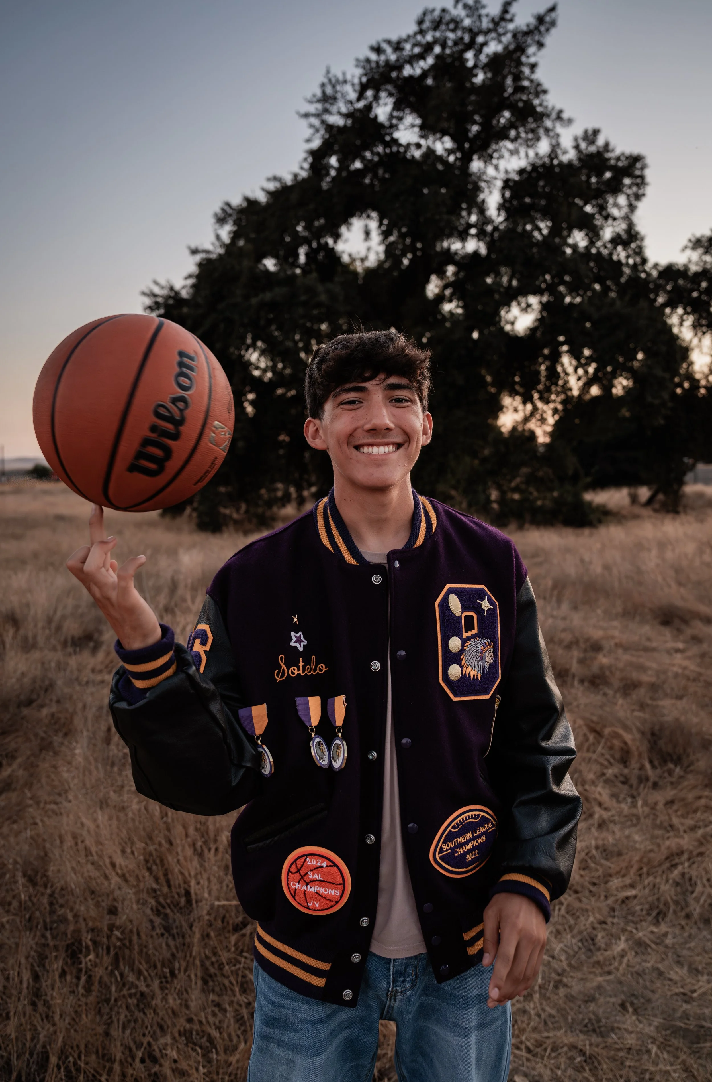 high school senior spinning a basketball on his finger while wearing his letterman. Photo taken in Newman, CA by Mikaela Tosta Photography