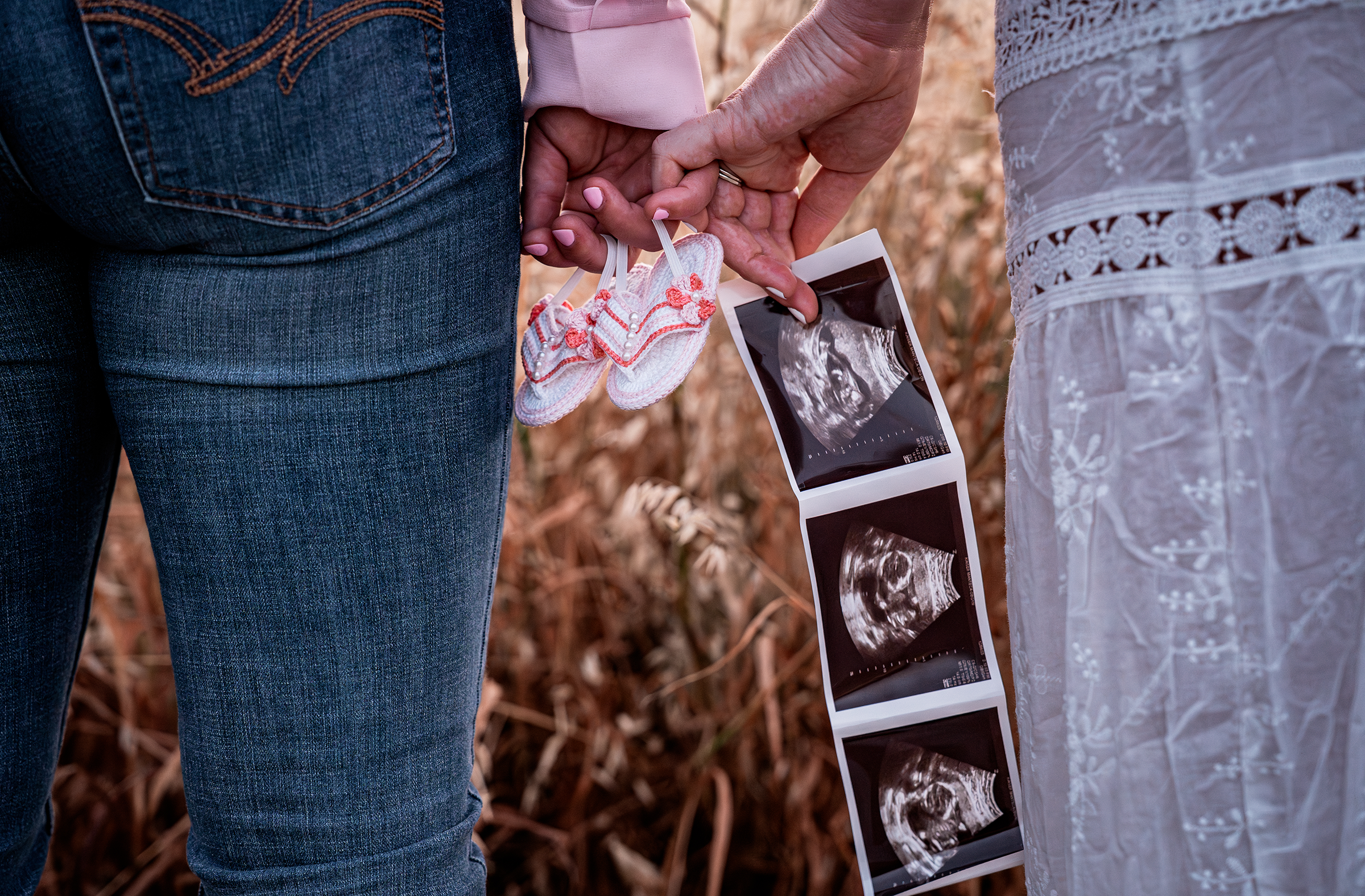 detail shot of moms holding hands, baby shoes and an ultrasound in an open field. Photo taken in Patterson, CA by Mikaela Tosta Photography.