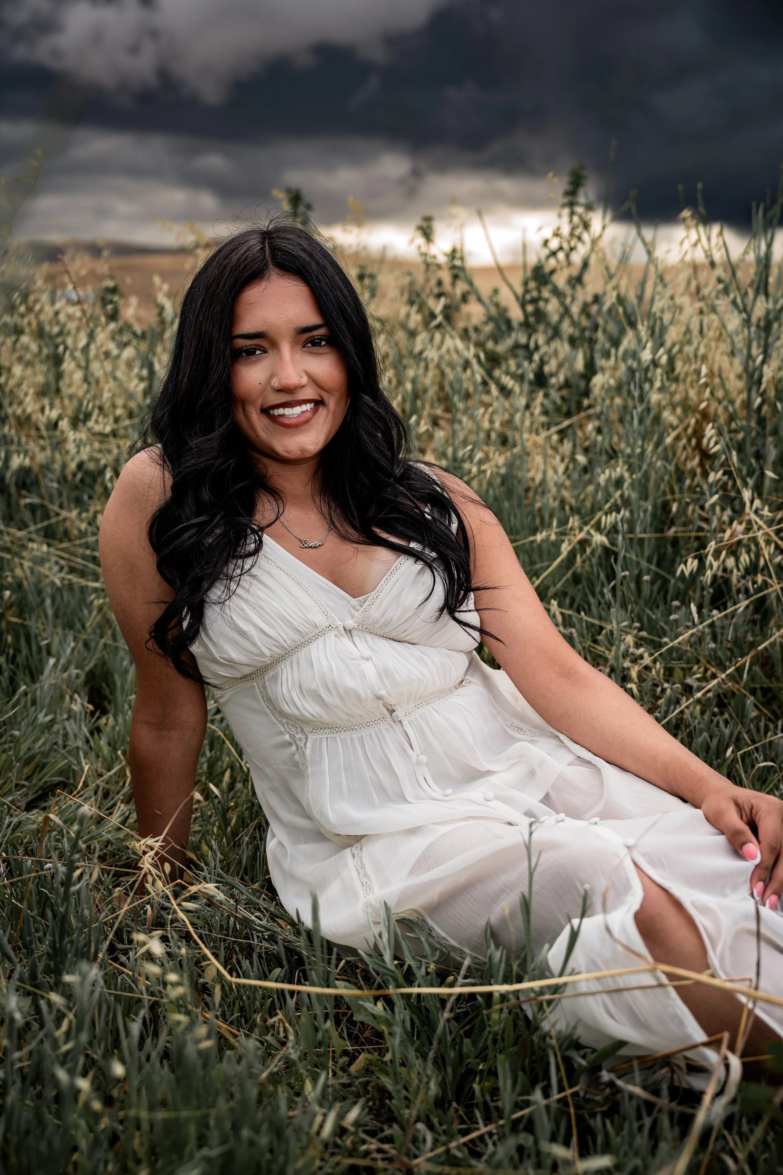 High school senior posing in a white dress while laying down in an open field. Photo taken in Patterson, CA by Mikaela Tosta Photography
