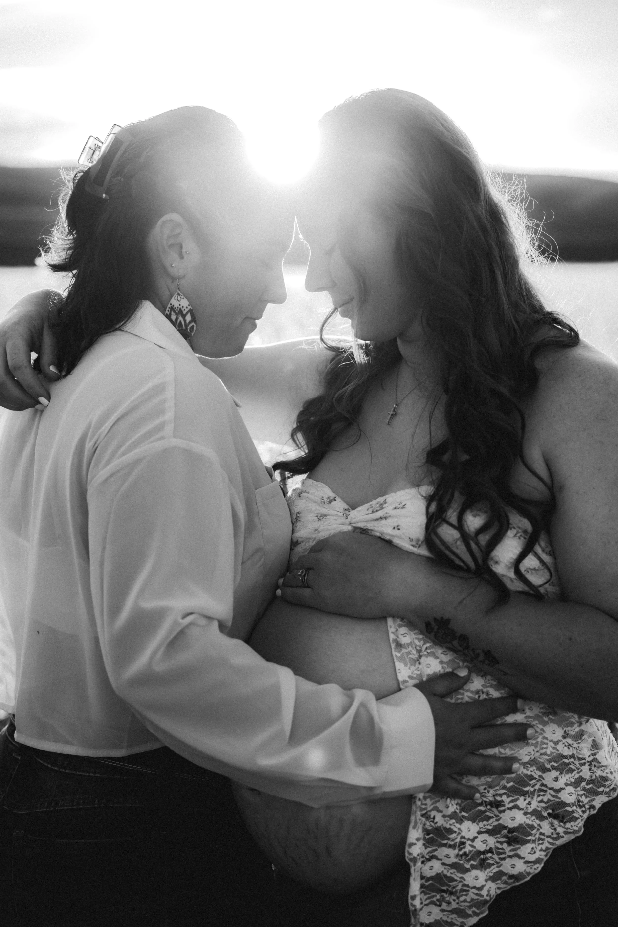 Black and white photo of pregnant mother snuggling with her wife in an open field. Photo taken in Patterson, CA by Mikaela Tosta Photography.