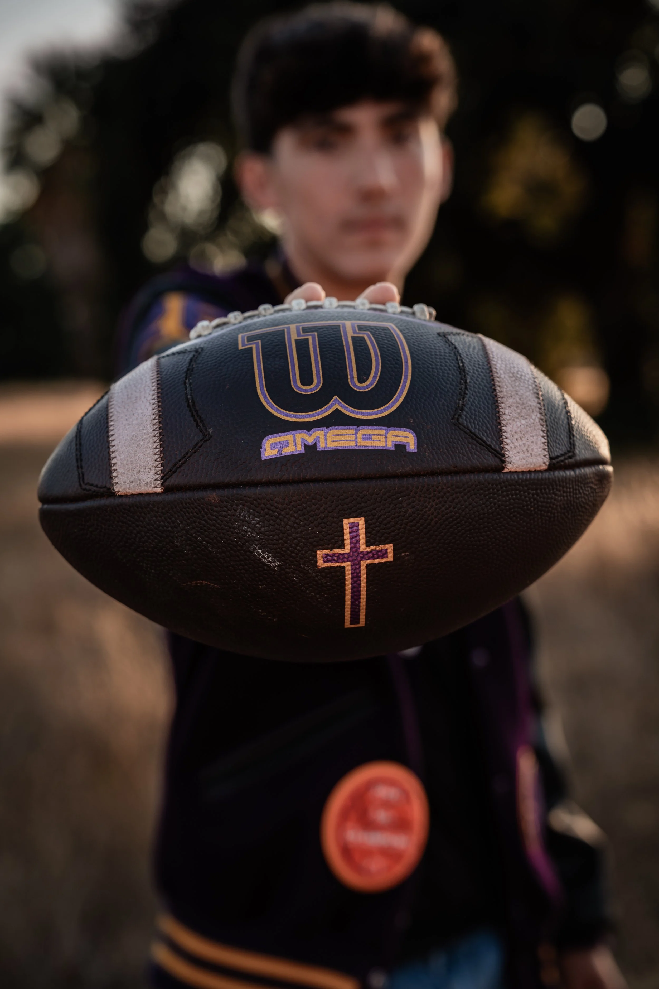 high school senior extended a football out while his face is blurred in the background. Photo taken in Newman, CA by Mikaela Tosta Photography