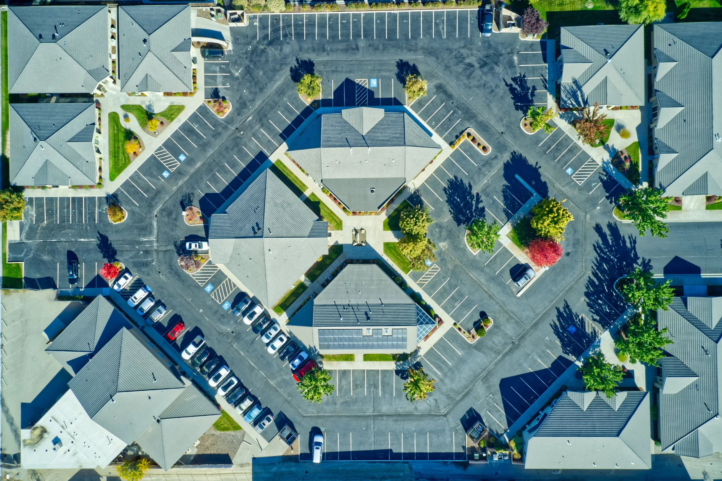 An aerial view of a parking lot surrounded by residential buildings with trees, some with colorful autumn foliage.