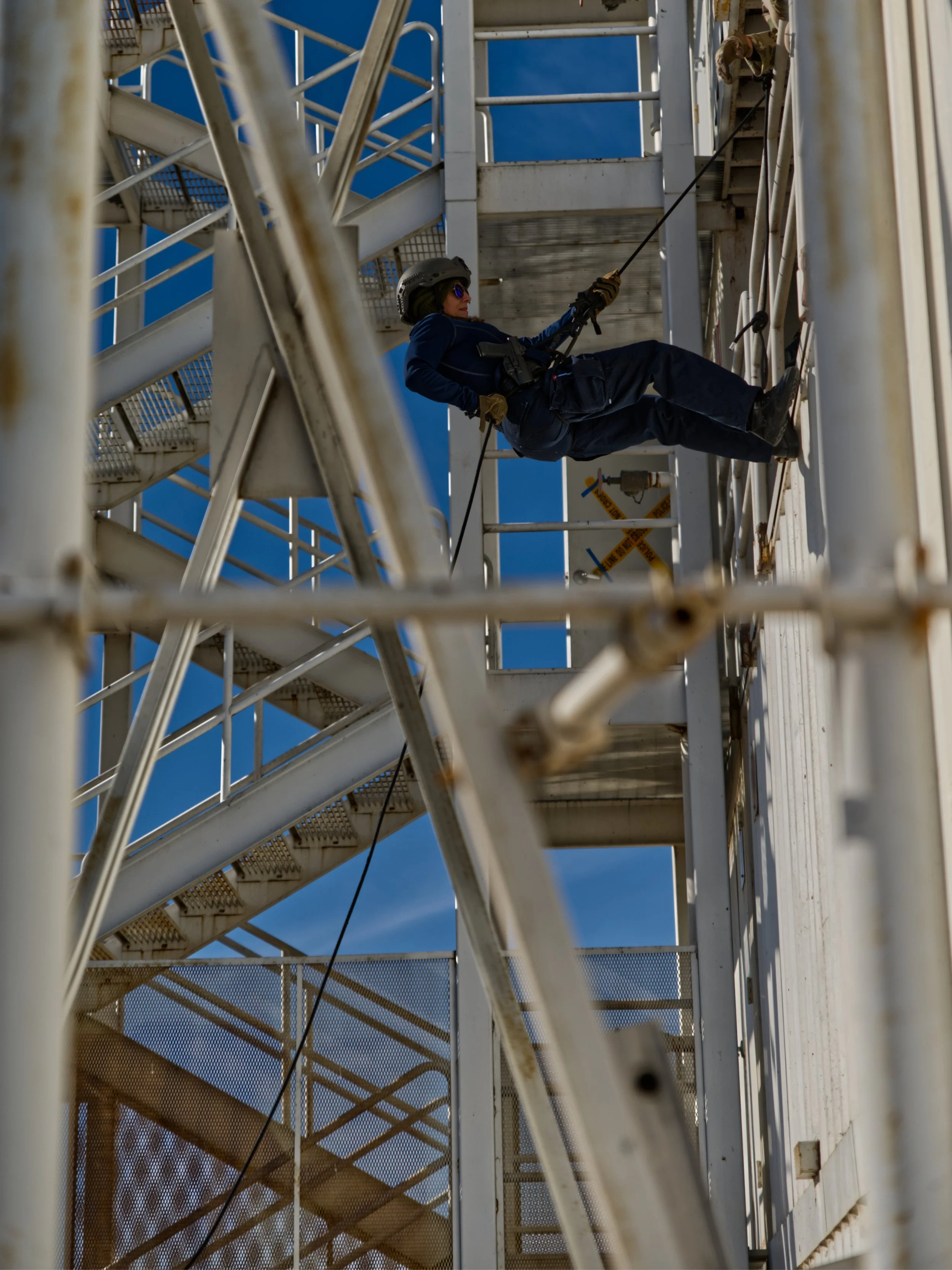 A worker in safety gear is rappelling down a metal fire escape structure.