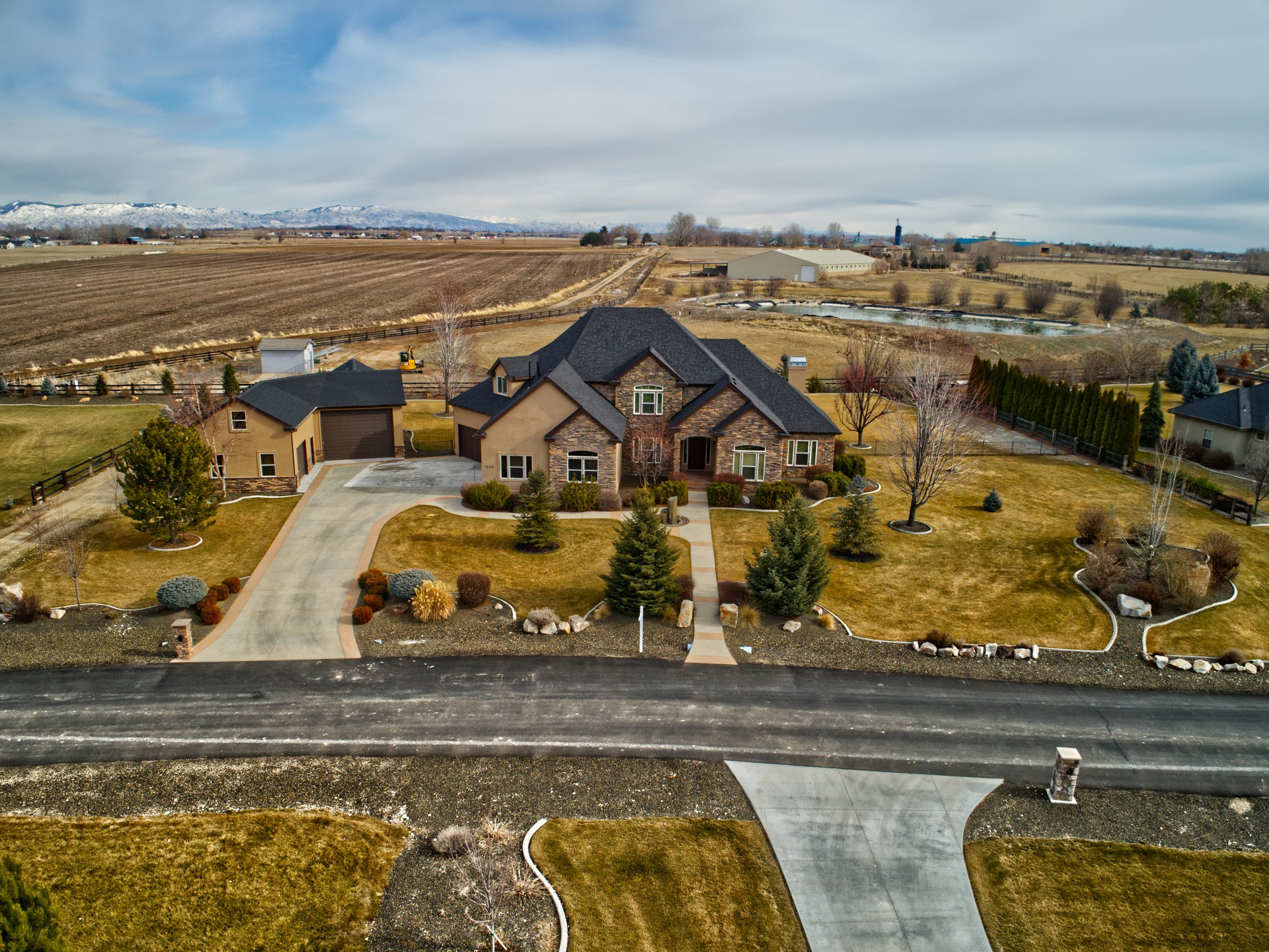 A view of a suburban house with a fenced yard, on a partly cloudy day, with a landscape of open fields, farms, and mountains in the background.