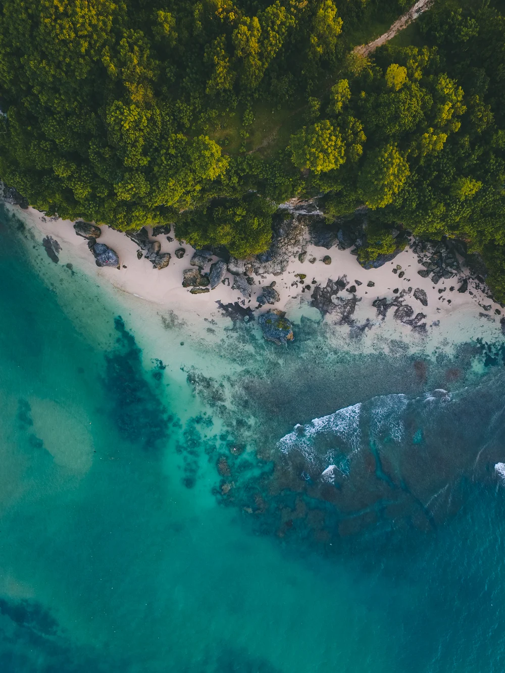 This drone capture of a beautiful coastline show the beautiful colors of nature. On the top of the frame is the green of the forest, whilst in the middle is the white sand that slowly fades into the light blue colors of the ocean. This photograph was taken in Indonesia, Bali, Padang Padang in 2018 By Oliver Sjöström, Ollivves