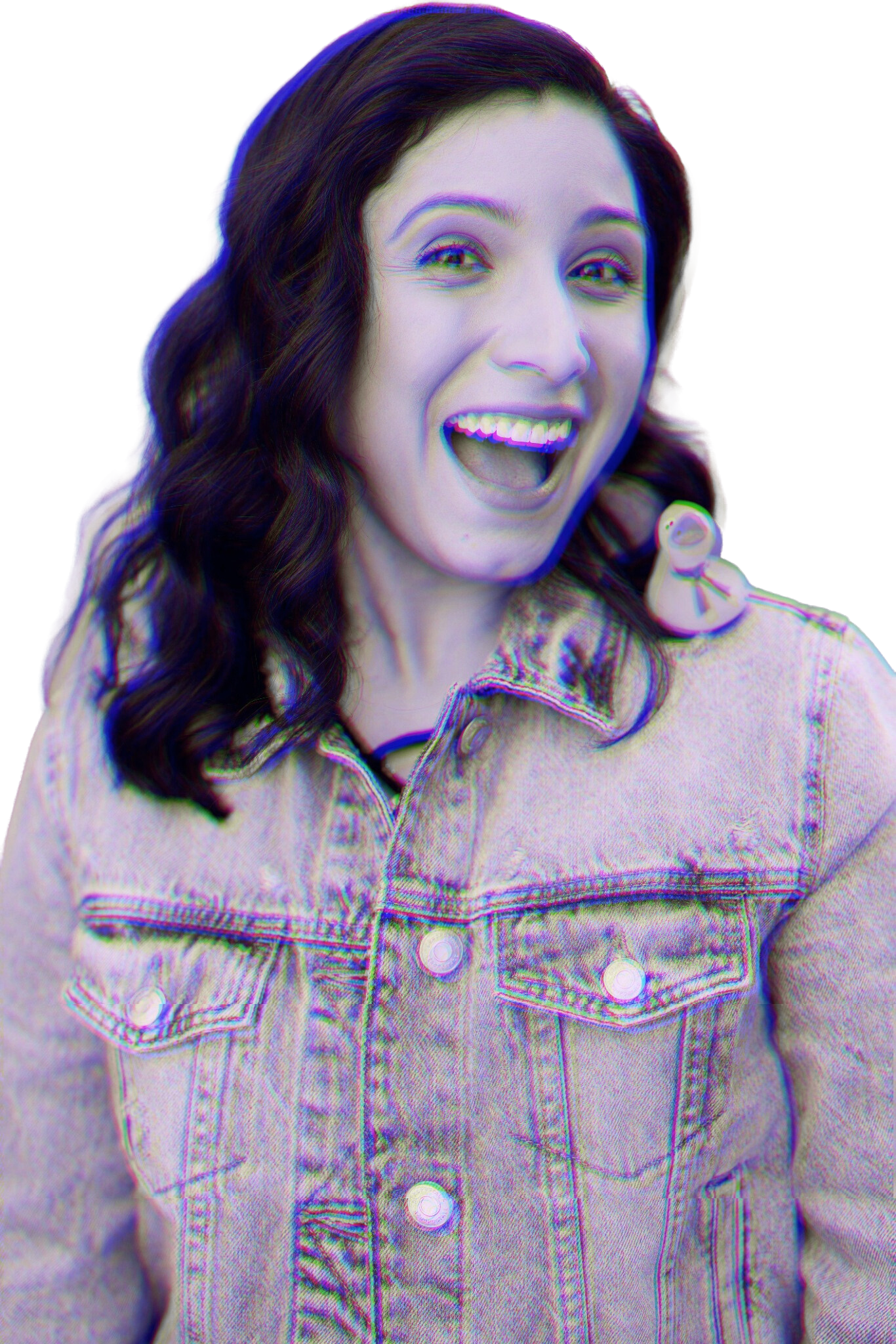 A young woman with dark wavy hair, wearing a denim jacket with a small doll attached to the shoulder, smiling and looking at the camera.