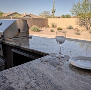 Outdoor kitchen with granite countertops and built-in grill in a desert backyard.