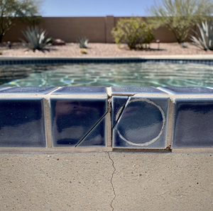 Cracked blue pool tiles above a cracked concrete deck, with desert landscaping behind.