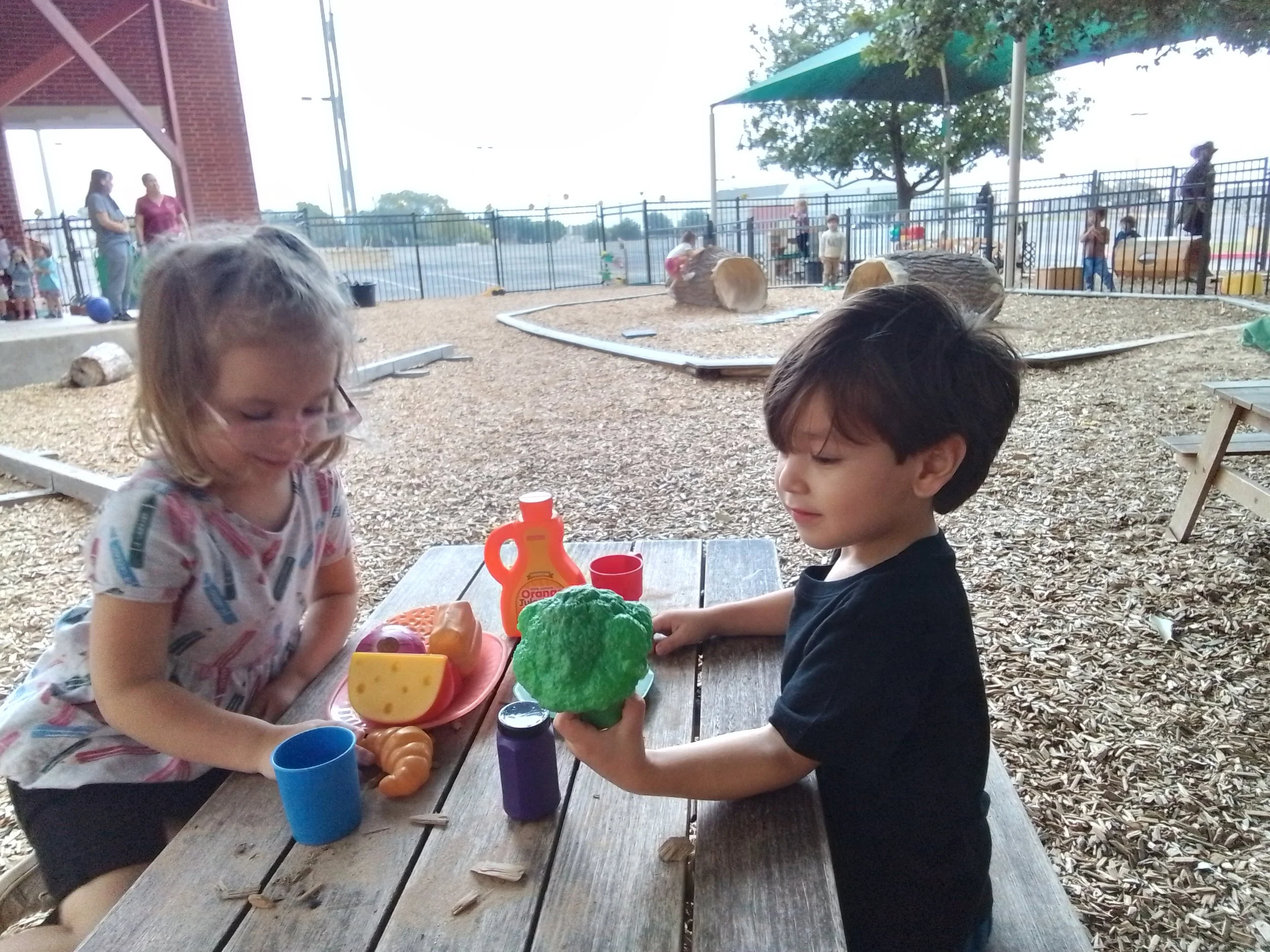 Two children are role playing restaurant outside on the playground