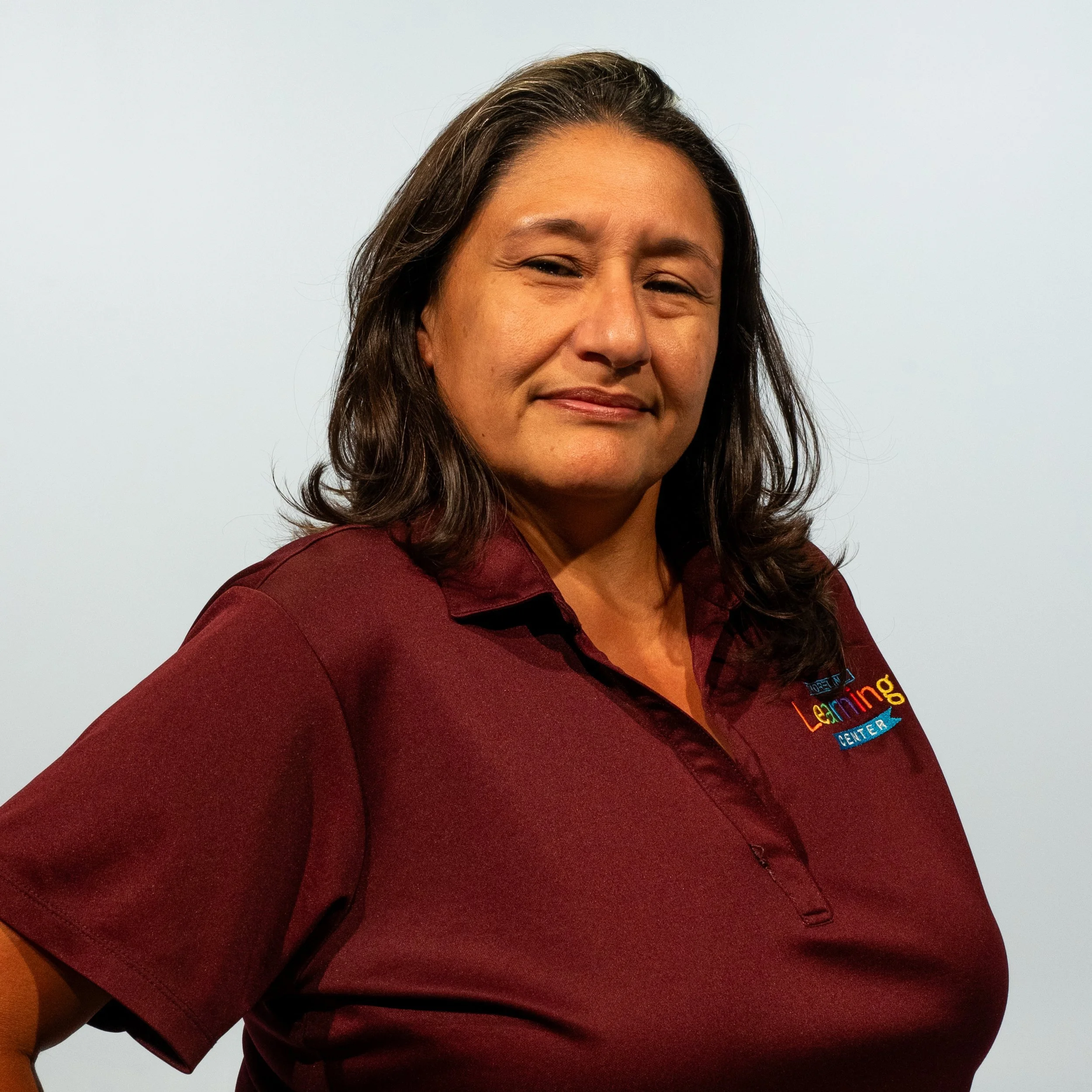 A woman with dark brown hair and a maroon polo shirt that says 'Learning Center' on the chest.
