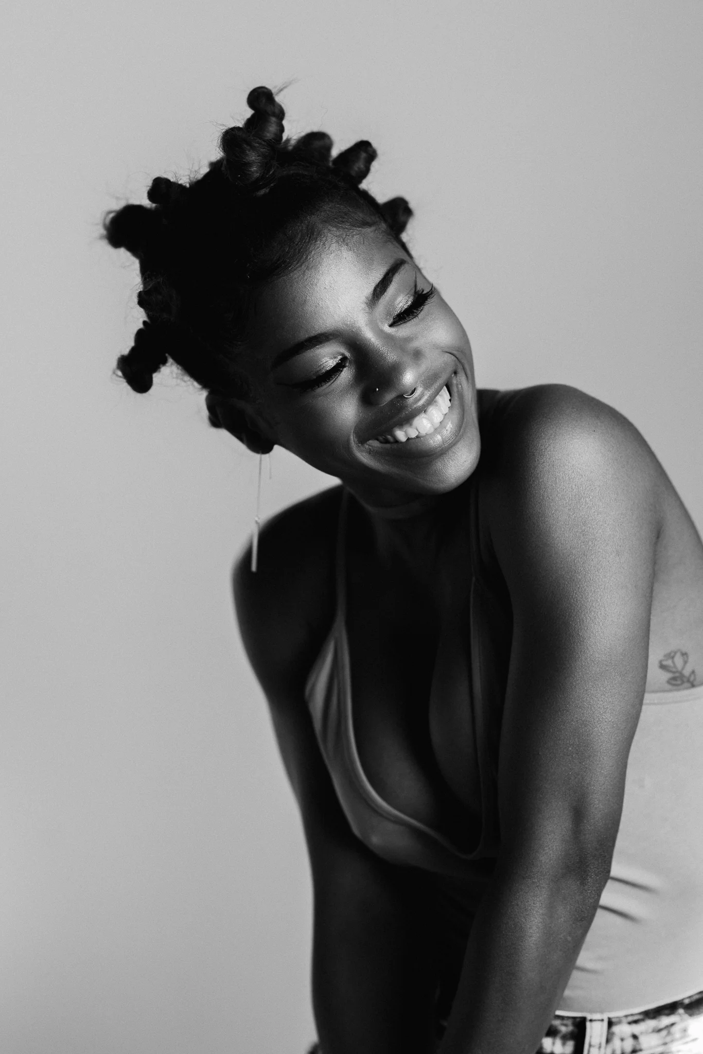 Black and white photo of a smiling woman with short, twisted hair, showing her teeth and looking downward.