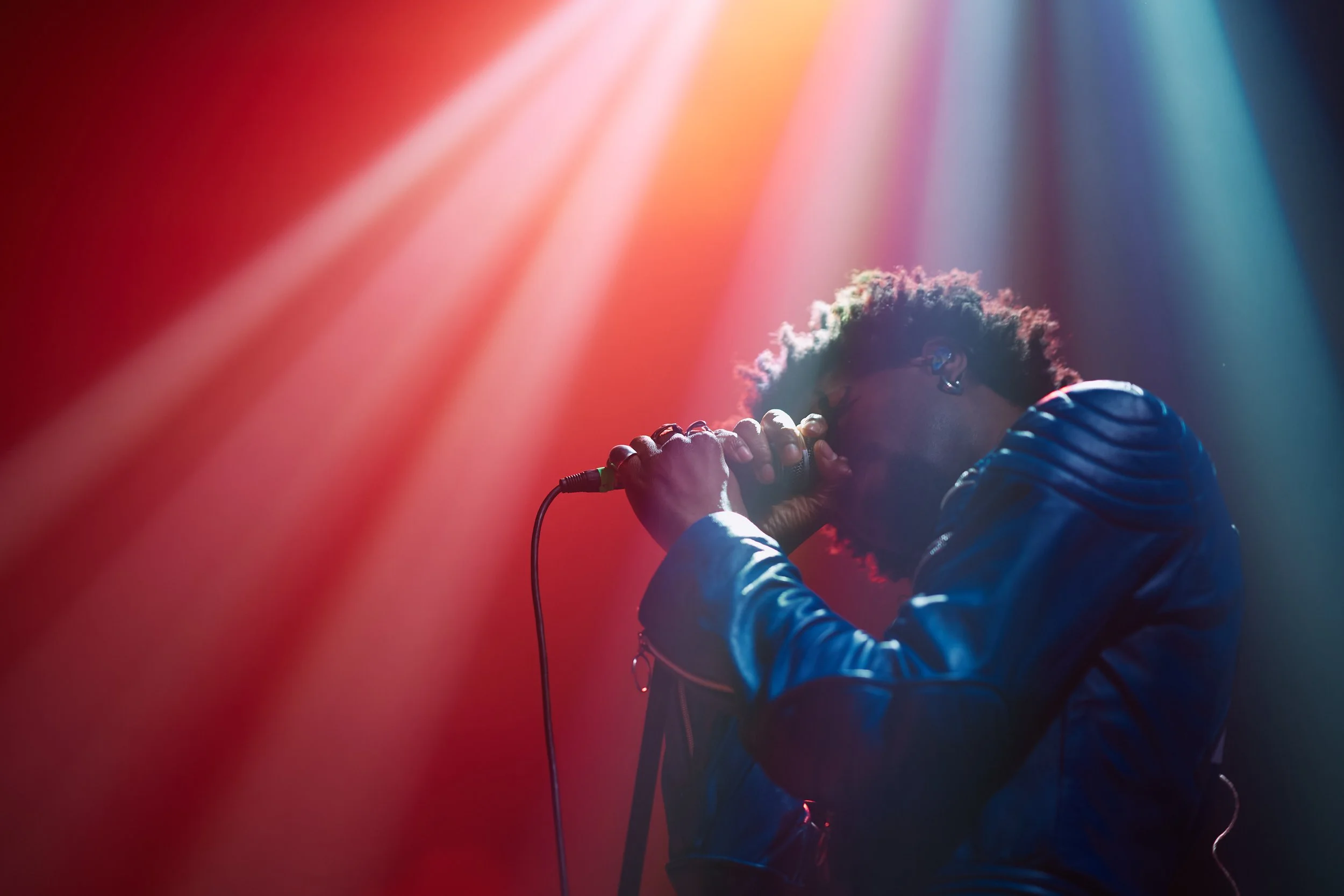A singer performing on stage holding a microphone with colorful stage lights shining down.