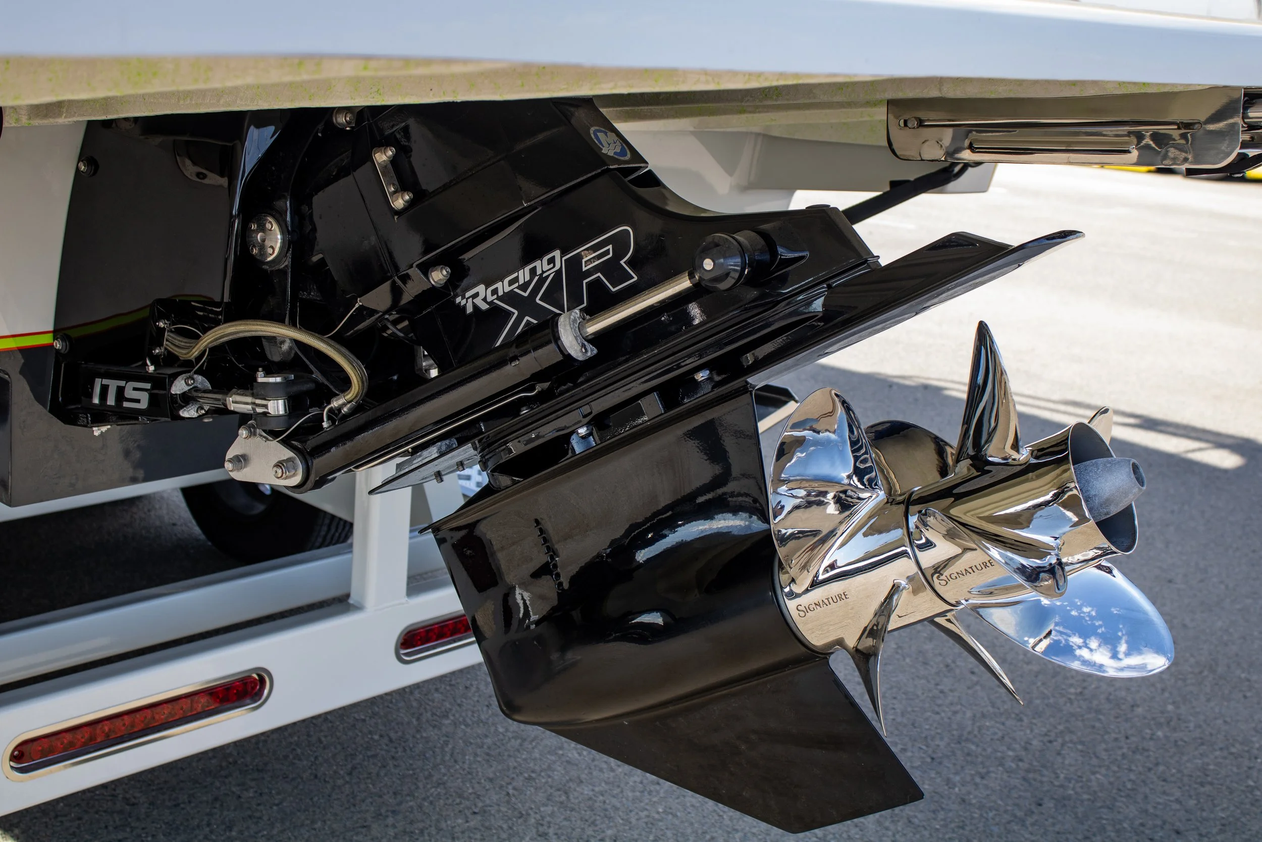 Close-up of a boat's engine and propeller, showing a black Racing XR outboard motor and a shiny, metallic propeller attached to the boat's stern.
