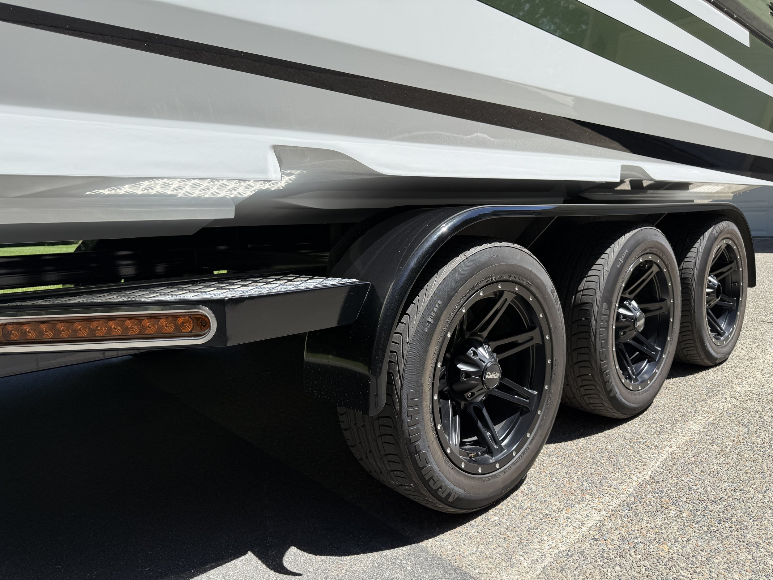 Close-up of a boat trailers side, showing black wheels and tires, with a part of the white and black trailer body visible.