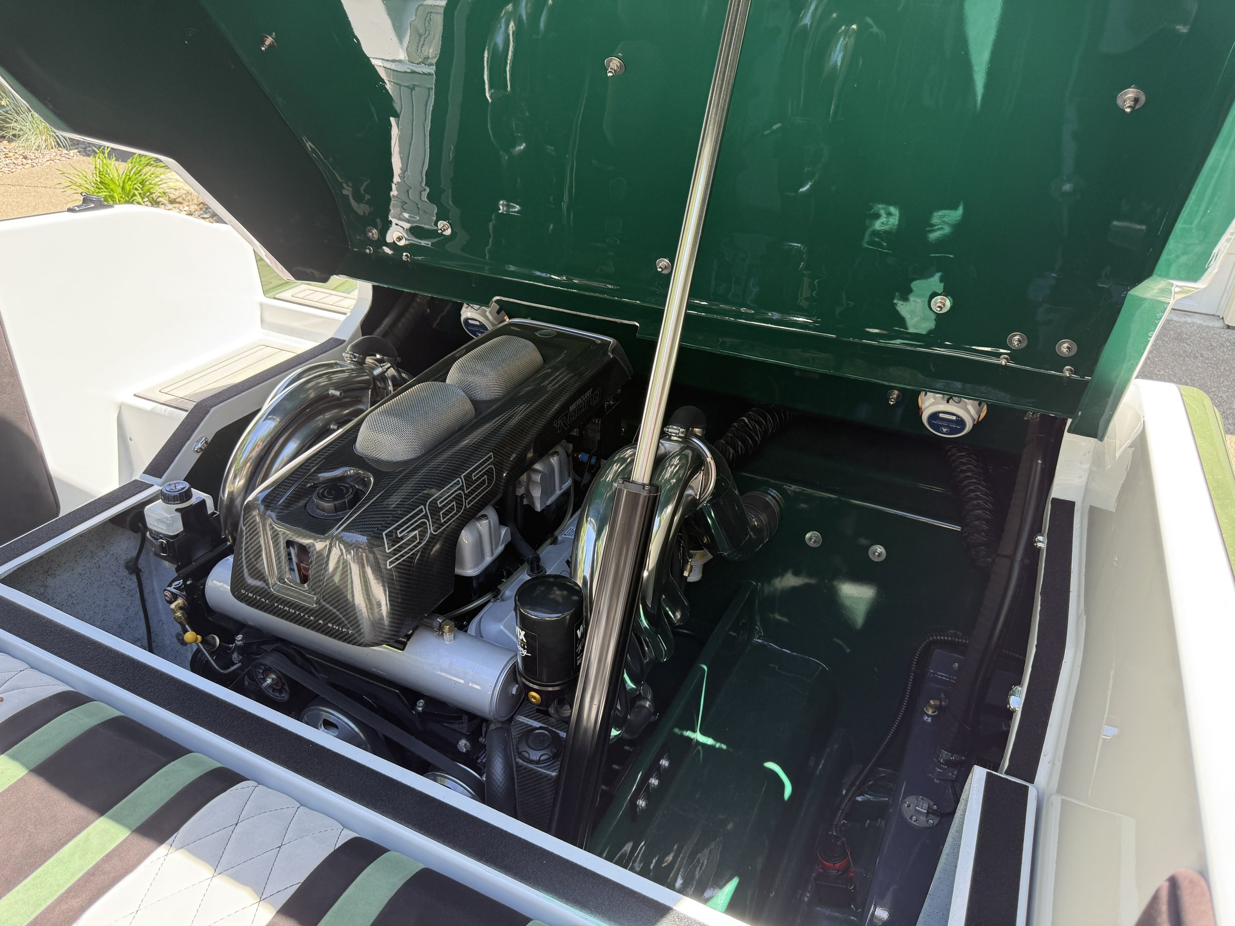 Close-up view of a racing car's engine inside its hood, with a black and green interior and visible mechanical components.