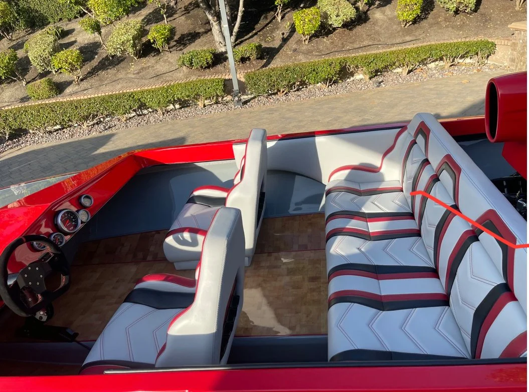 The interior of a vintage red and white boat showing white seating with red and black accents, dashboard with gauges, and a steering wheel.