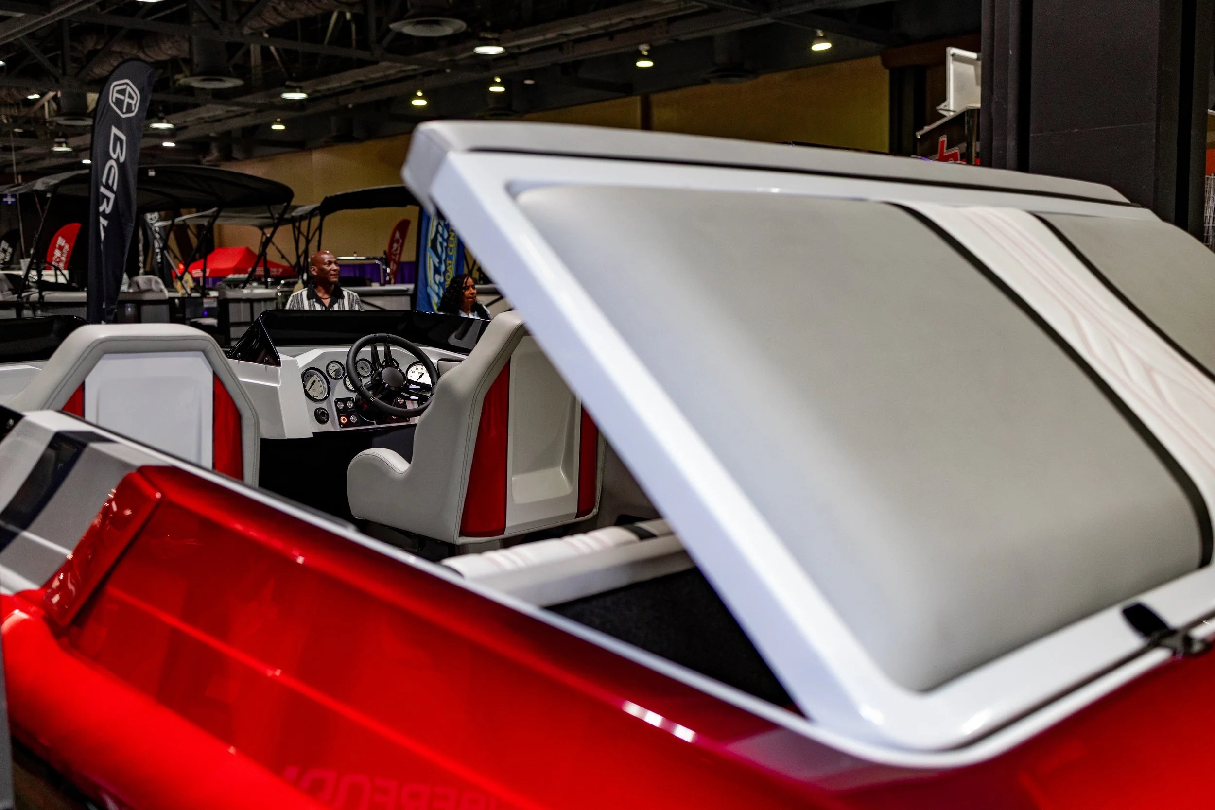 Interior of a red and white boat with white and red seats and a steering wheel, displayed at an indoor boat show.