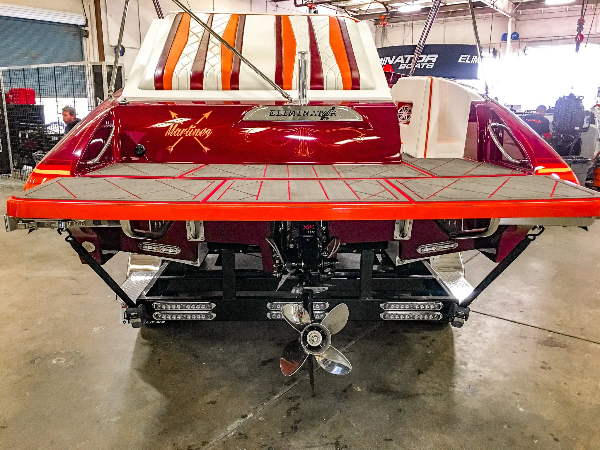 Front view of a speedboat with a red and white paint job, featuring the names 'Martinez' and 'Eliminator' on the hull, inside a warehouse.