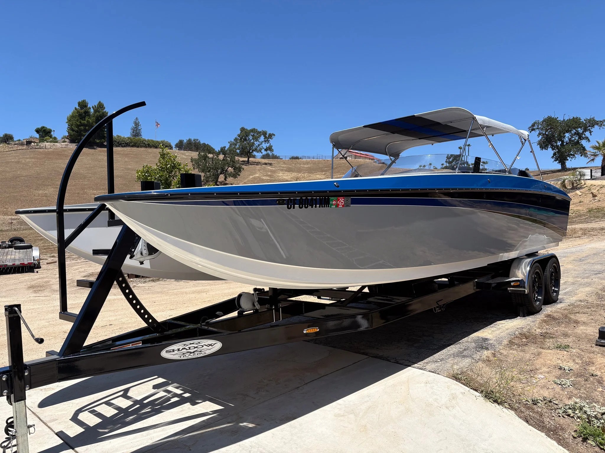 A speedboat on a black trailer at an outdoor location with blue sky, trees, and a hill with an American flag in the background.