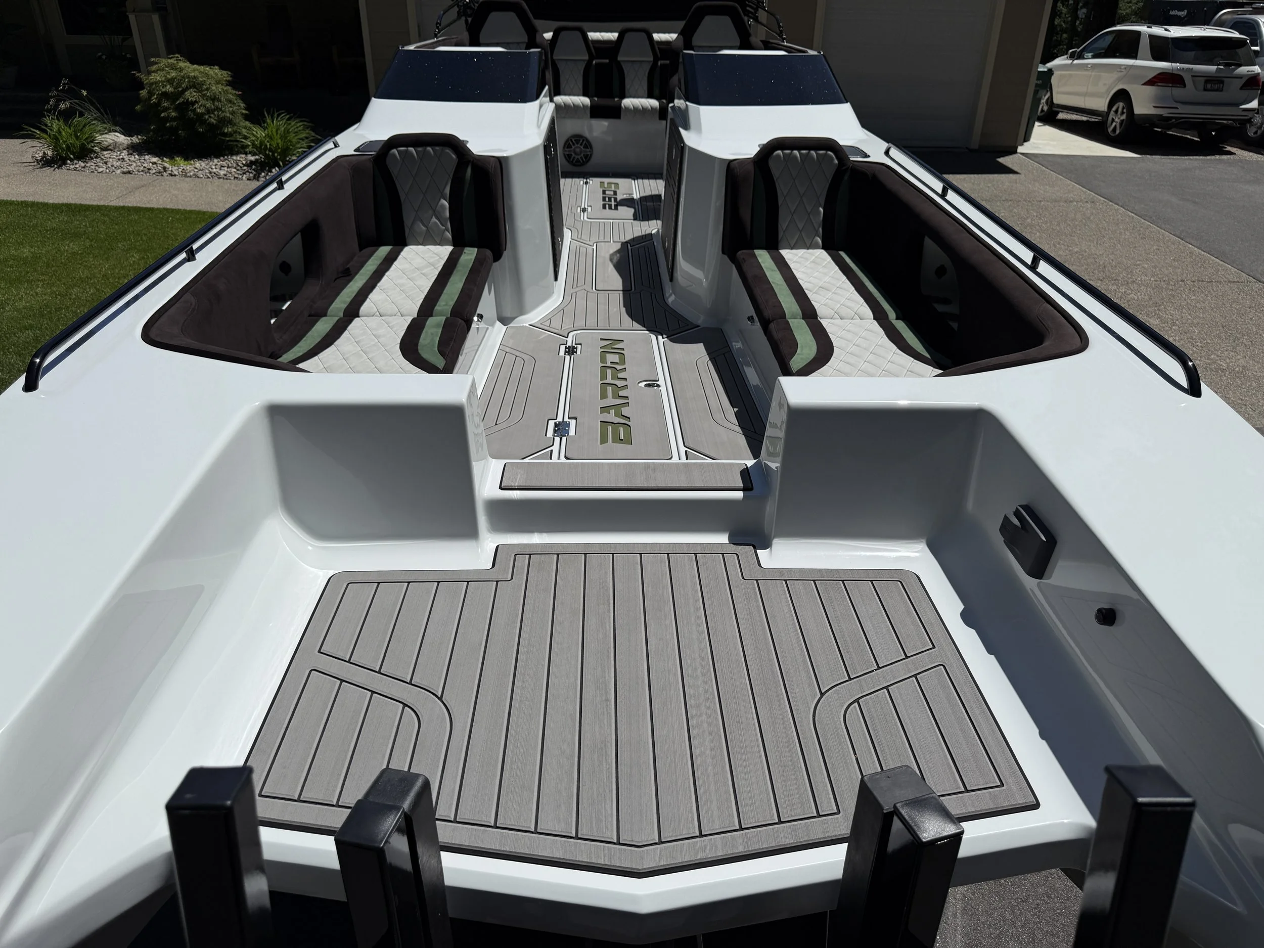 View of a white motorboat's interior, showing seating with black and green cushions, a gray deck, and black safety rails, parked outdoors in a driveway.