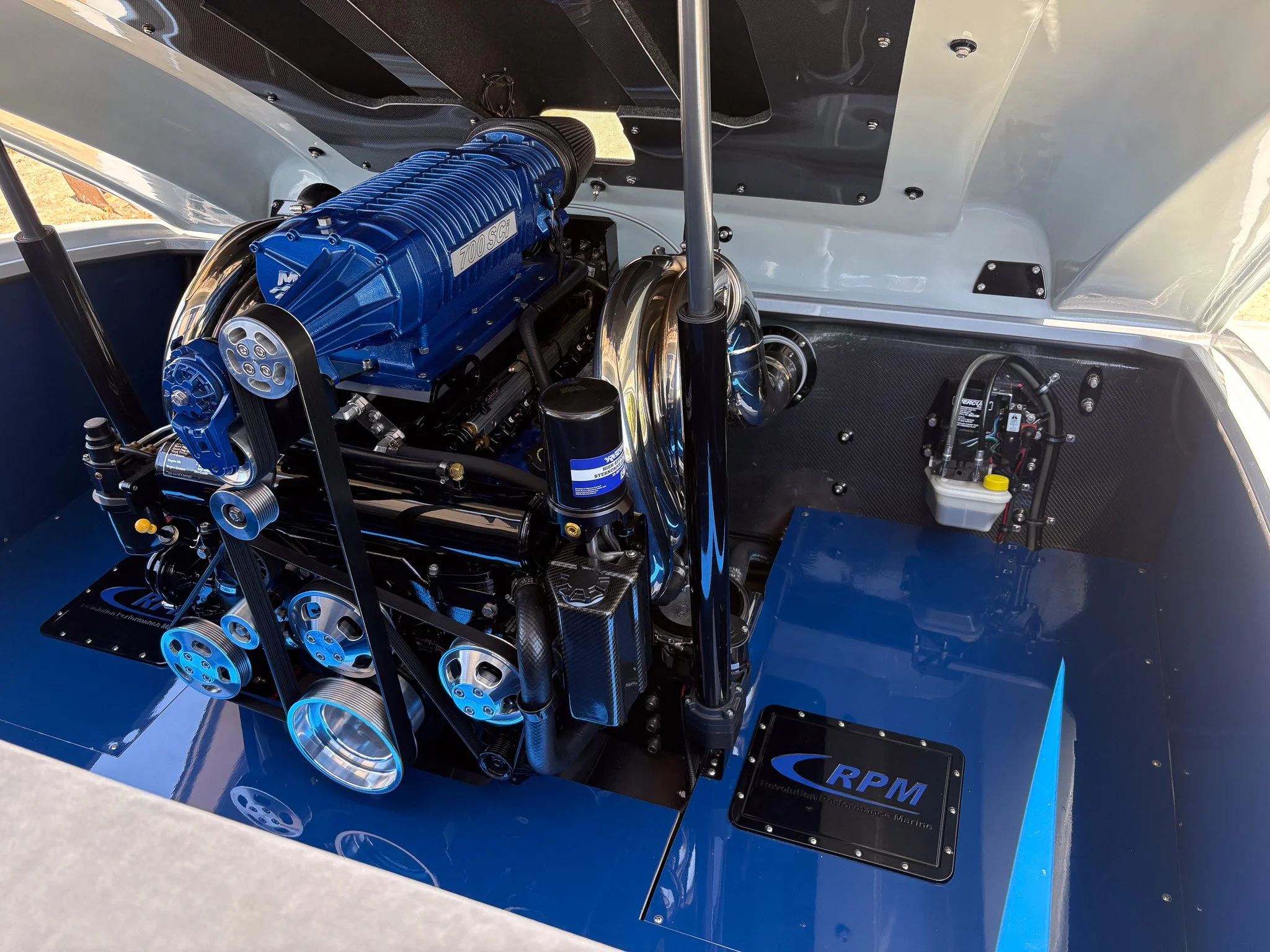 Close-up of a boat engine with a blue cover labeled '700 SCI'. The engine is inside a boat with a black floor featuring some mechanical components and wiring visible.