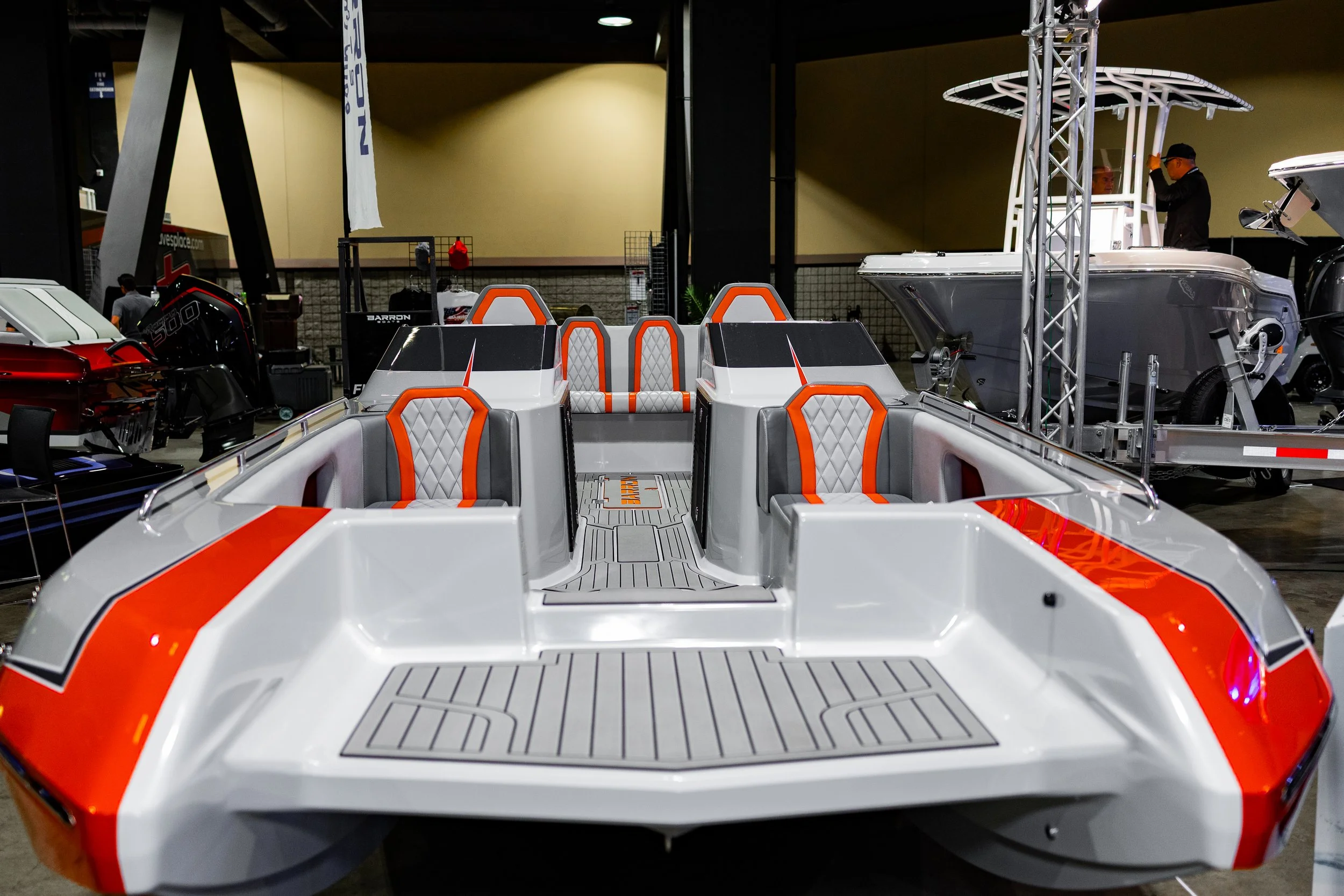View of a boat with white and orange seats, displayed indoors at an exhibition.