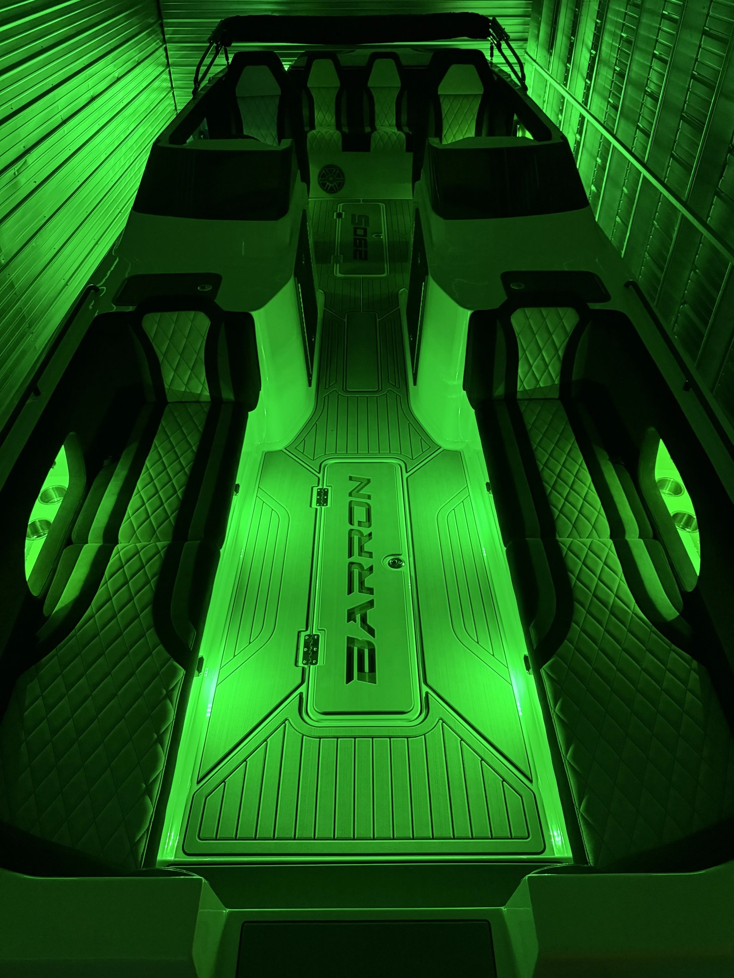Interior of a futuristic boat with seating and flooring illuminated by green LED lights, with the word 'BARRON' on the floor.