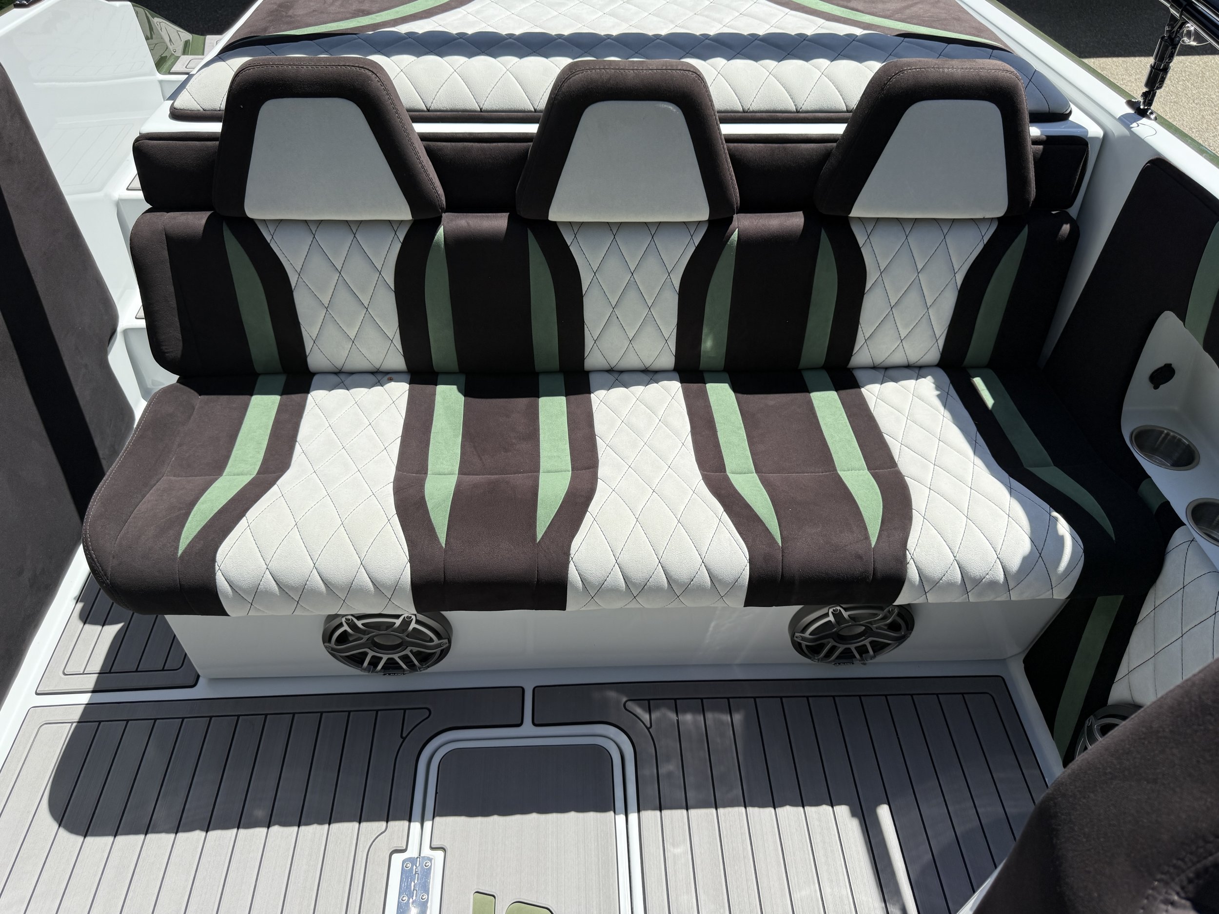 The interior of a boat with a white and black quilted seat backrest, three headrests, and a colorful woven blanket or cushion. The boat floor features a textured, non-slip surface with metal fittings.