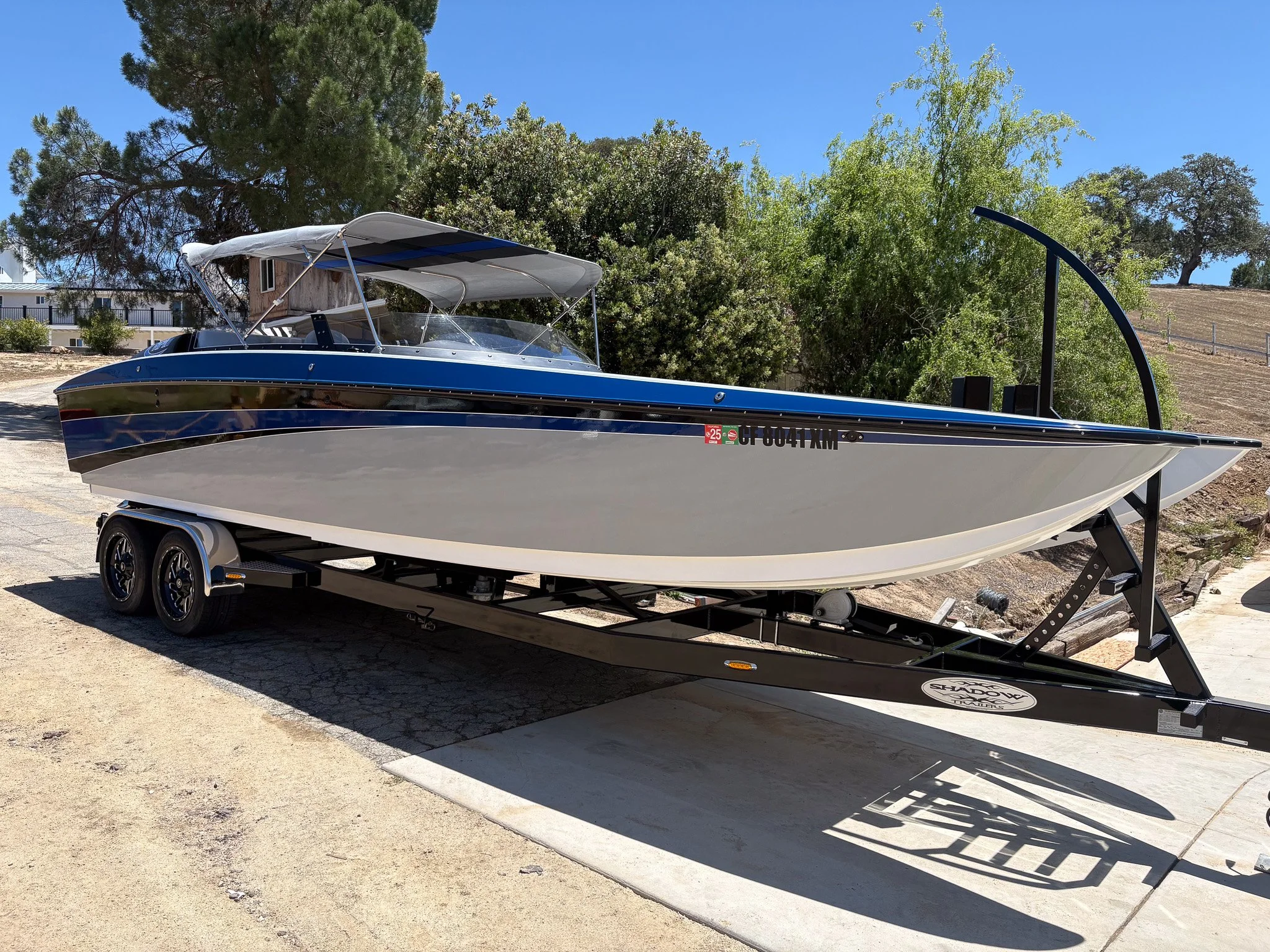A speedboat mounted on a trailer parked on a concrete ground with trees and a blue sky in the background.