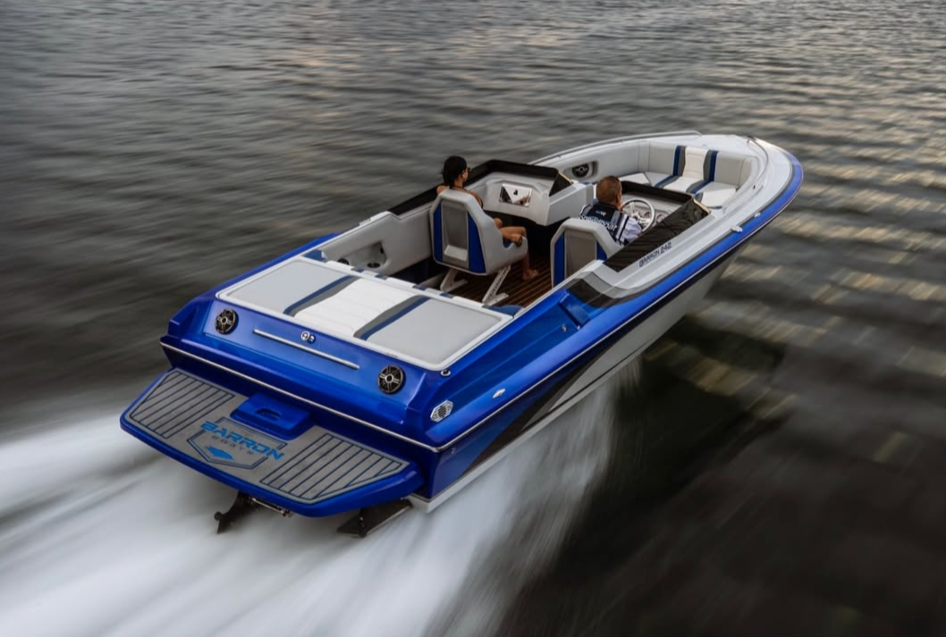 Blue and white speedboat with two people on board, moving quickly across the water during sunset or sunrise.