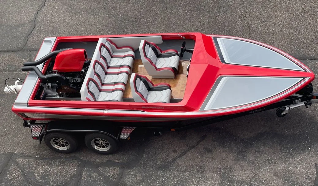A small red boat with white and gray striped seats, a steering wheel, and an attached jet, parked on a trailer on pavement.