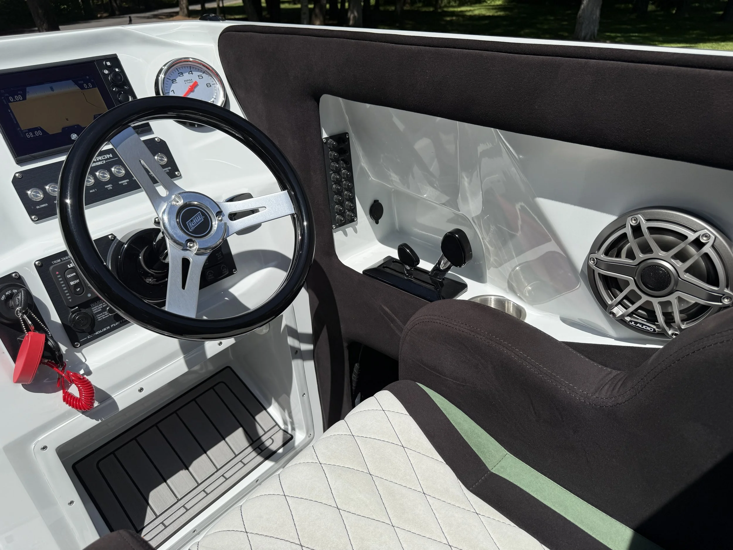 The cockpit of a small boat, showing a steering wheel, a range of gauges and controls, a speaker, and a cushioned seat with a striped pattern.