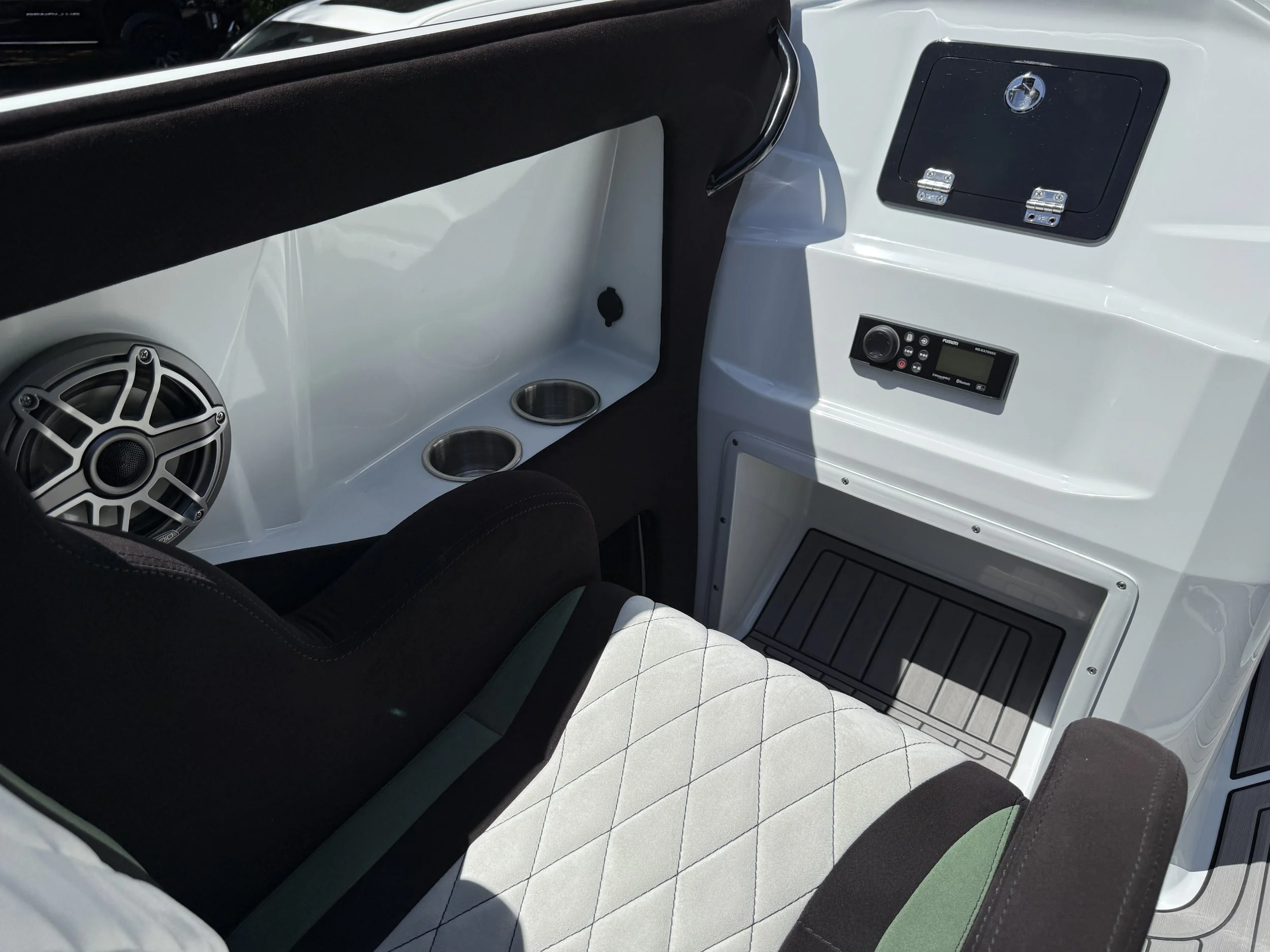Interior of a boat or yacht with a black and white color scheme, featuring a large speaker, two cup holders, a black control panel, and a storage compartment with a lock.