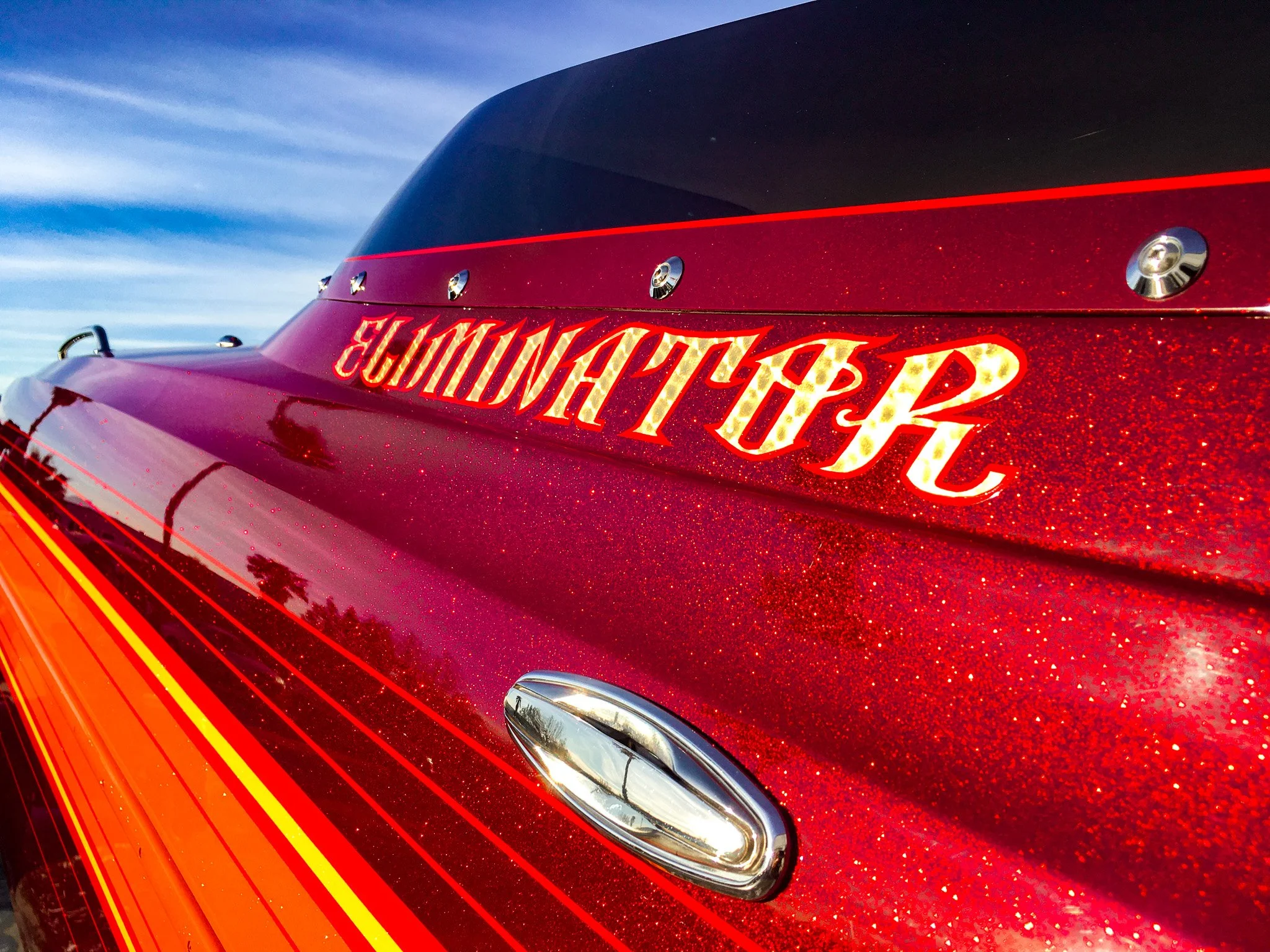 Close-up of a red sports car with glittery paint finish, featuring a decorative decal reading 'SHAKAAH 48' in bright lights, and a shiny silver bumper.