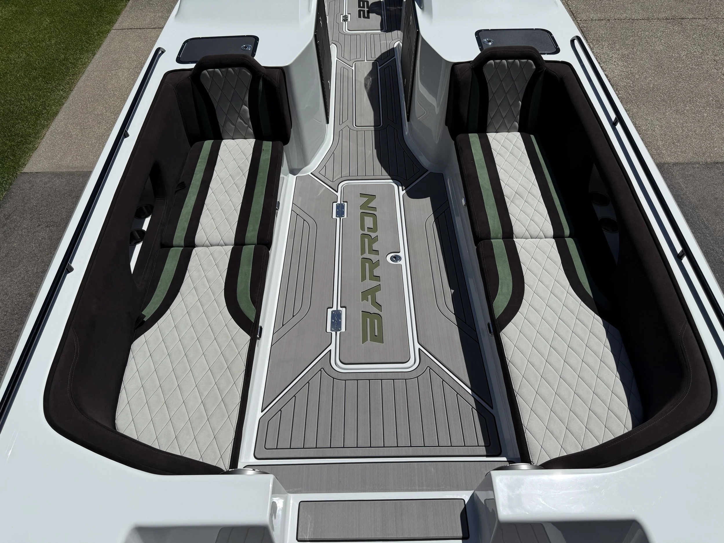 Top view of a boat's interior showing two black cushioned seats with diamond pattern stitching, a gray floor with textured pattern, and a central hatch with the word 'BARRON' on it.