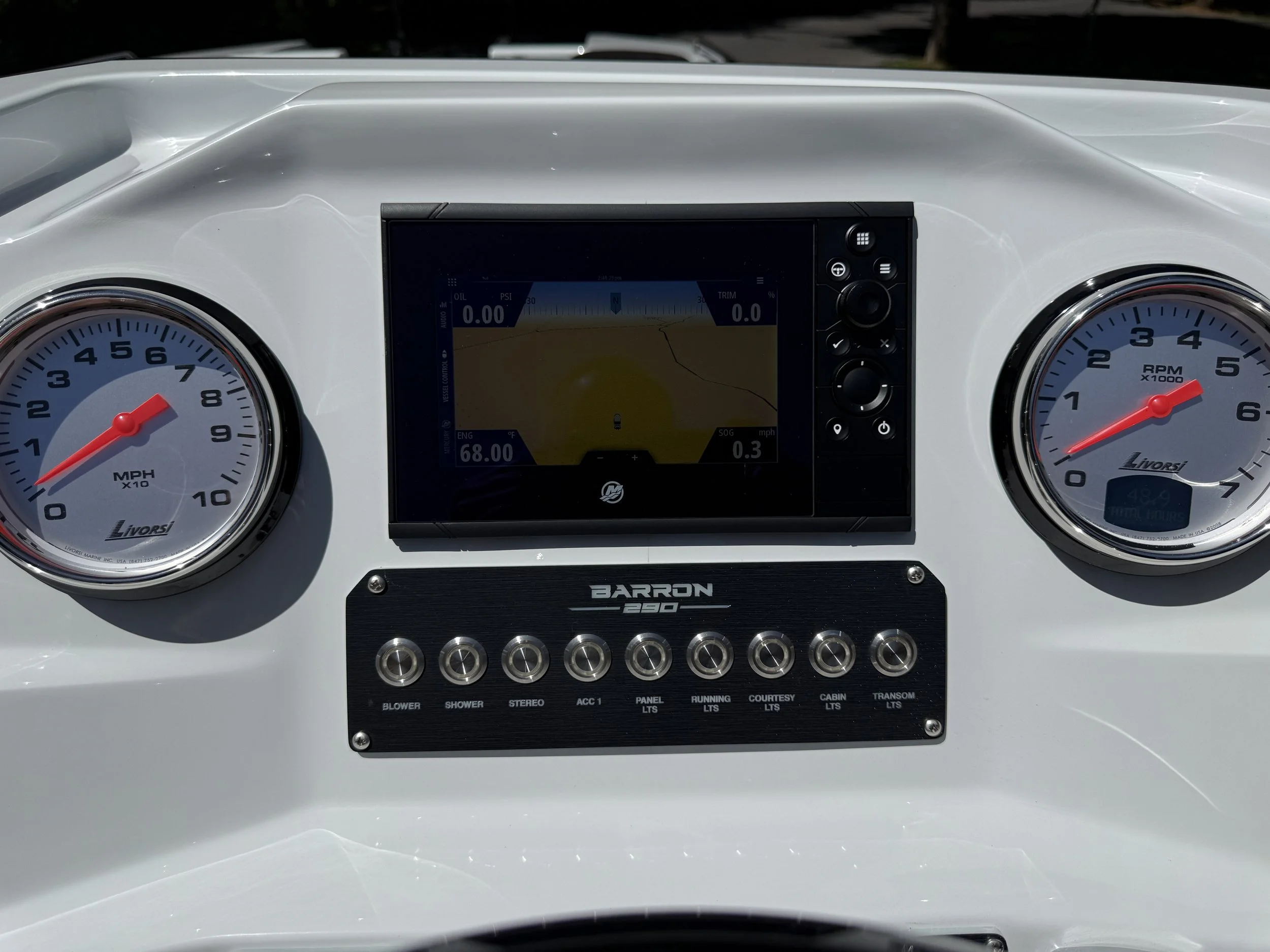 Dashboard of a boat with two large gauges showing MPH and RPM, a digital navigation screen in the center, and labels for various boat systems below.