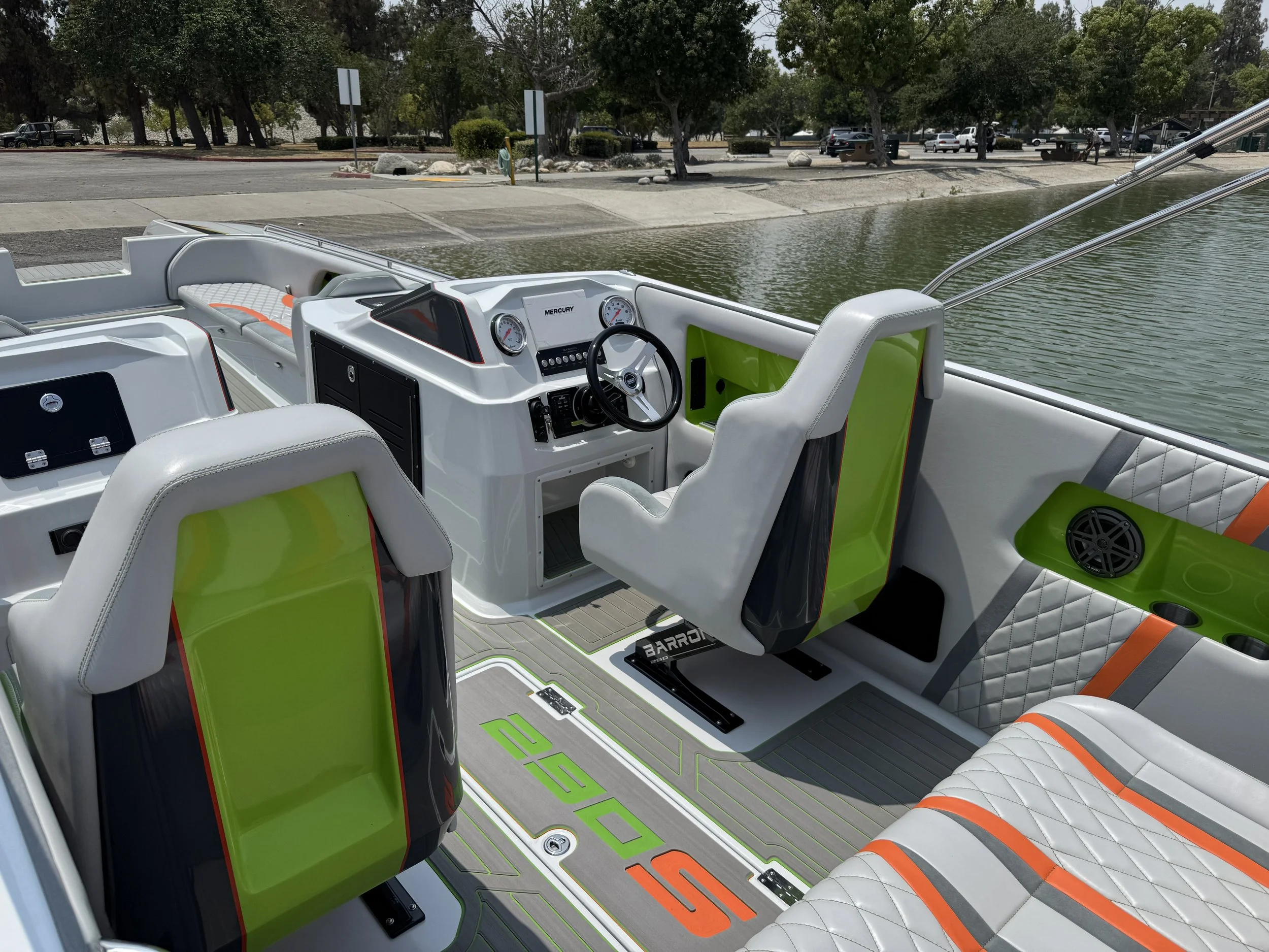 Interior of a modern boat with white seats accented with lime green and orange details, the boat is docked near a park with trees and water visible in the background.