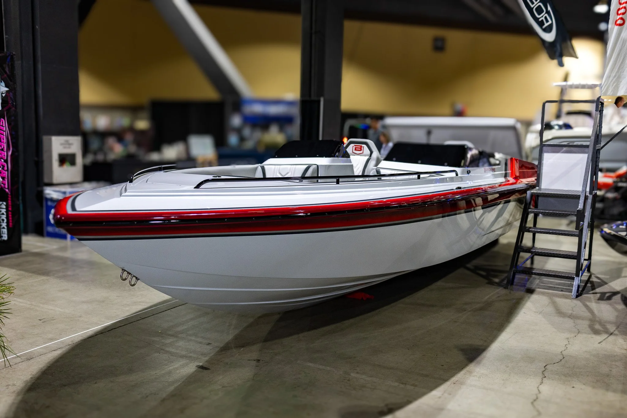 A detailed model of a white speedboat with black and red accents displayed indoors, with some ladders and other items nearby.