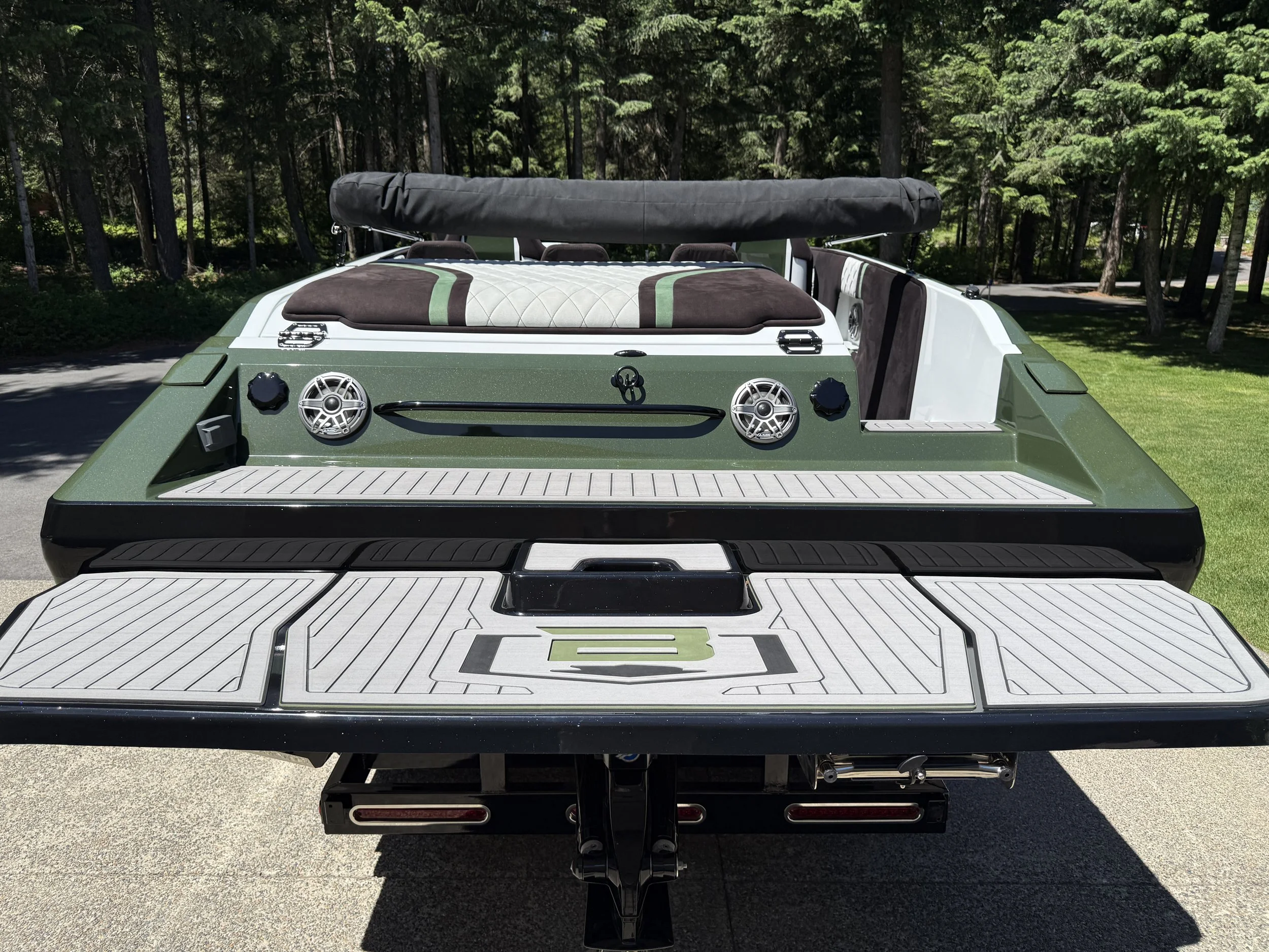 Rear view of a pontoon boat with fishing equipment and nearby trees.