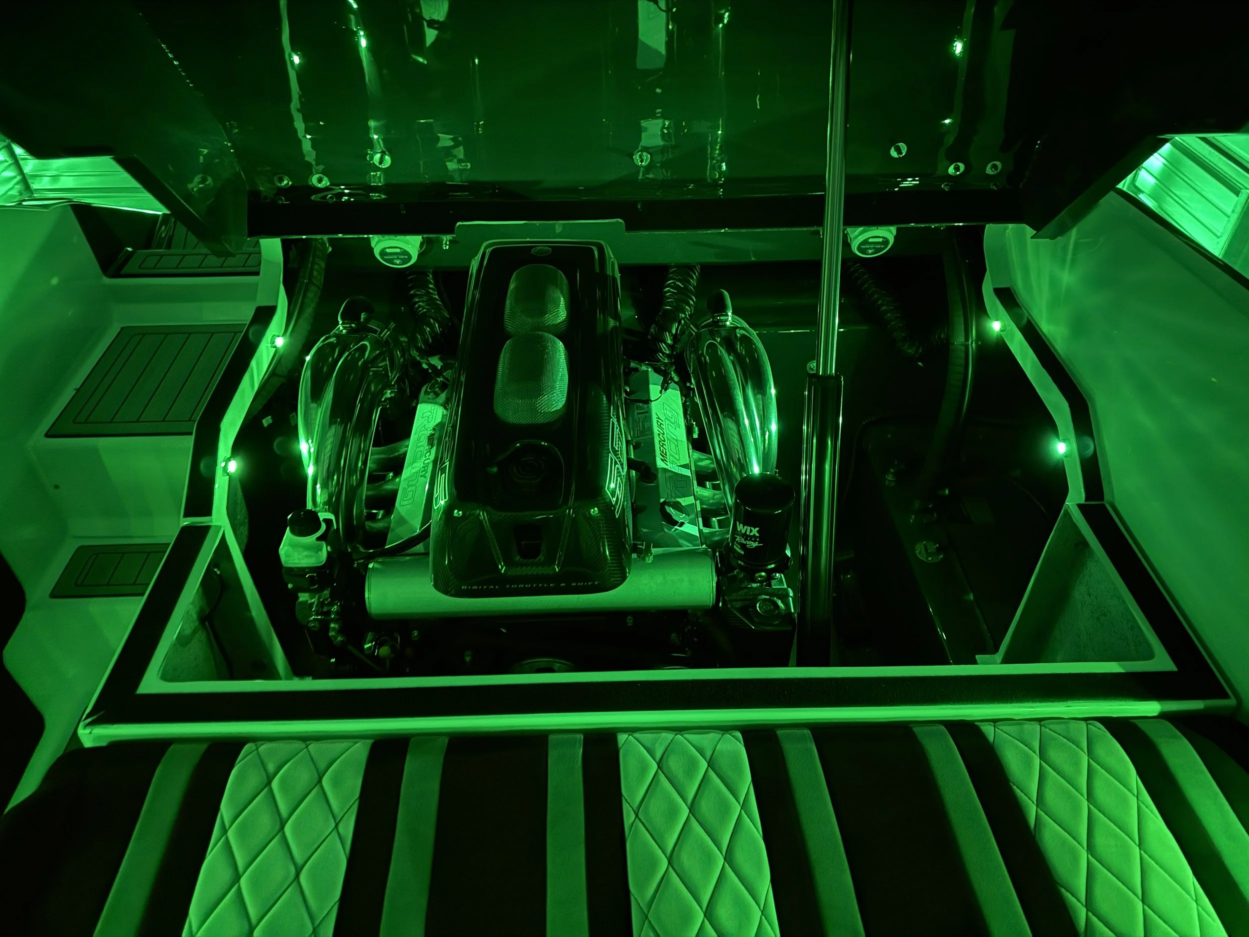 A racing car engine inside a transparent green-lit enclosure, with visible metal pipes and components.
