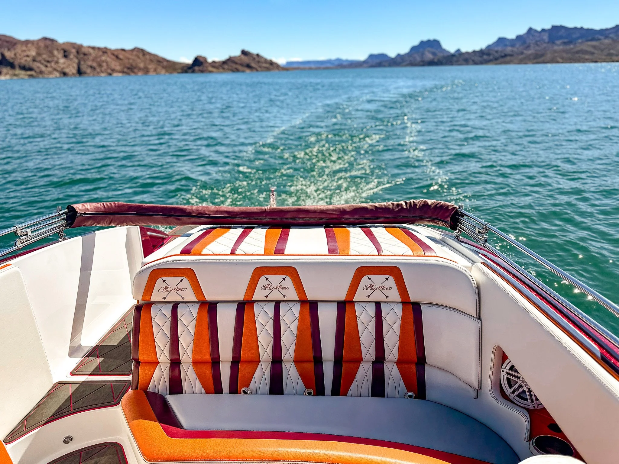 View from a boat showing colorful cushioned seating area with mountains and blue sky in the background.