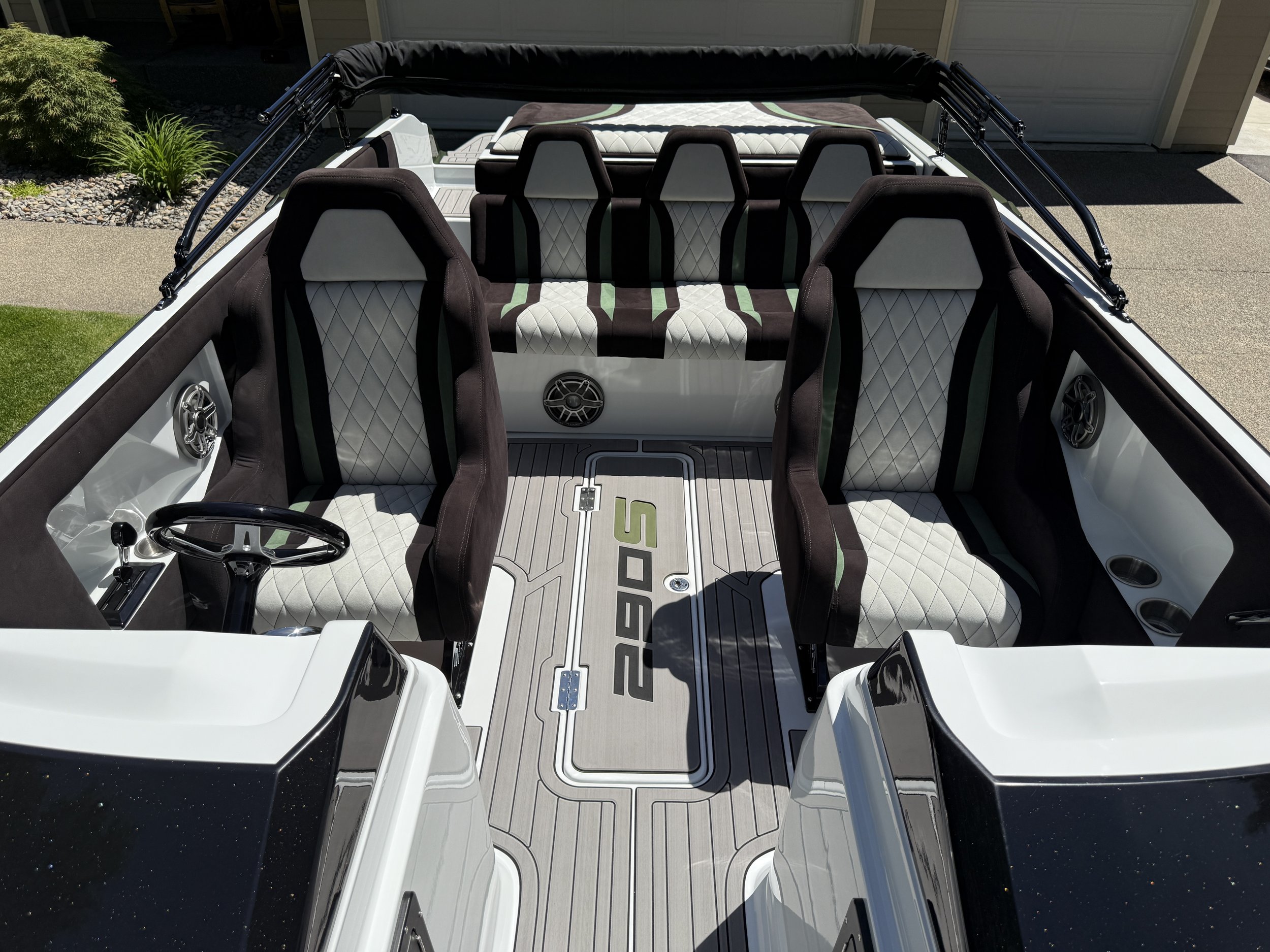 View from above of a luxury boat's seating area with black and white diamond-stitched upholstery, a beige and black floor, and mounted speakers on the sides, parked in a driveway.