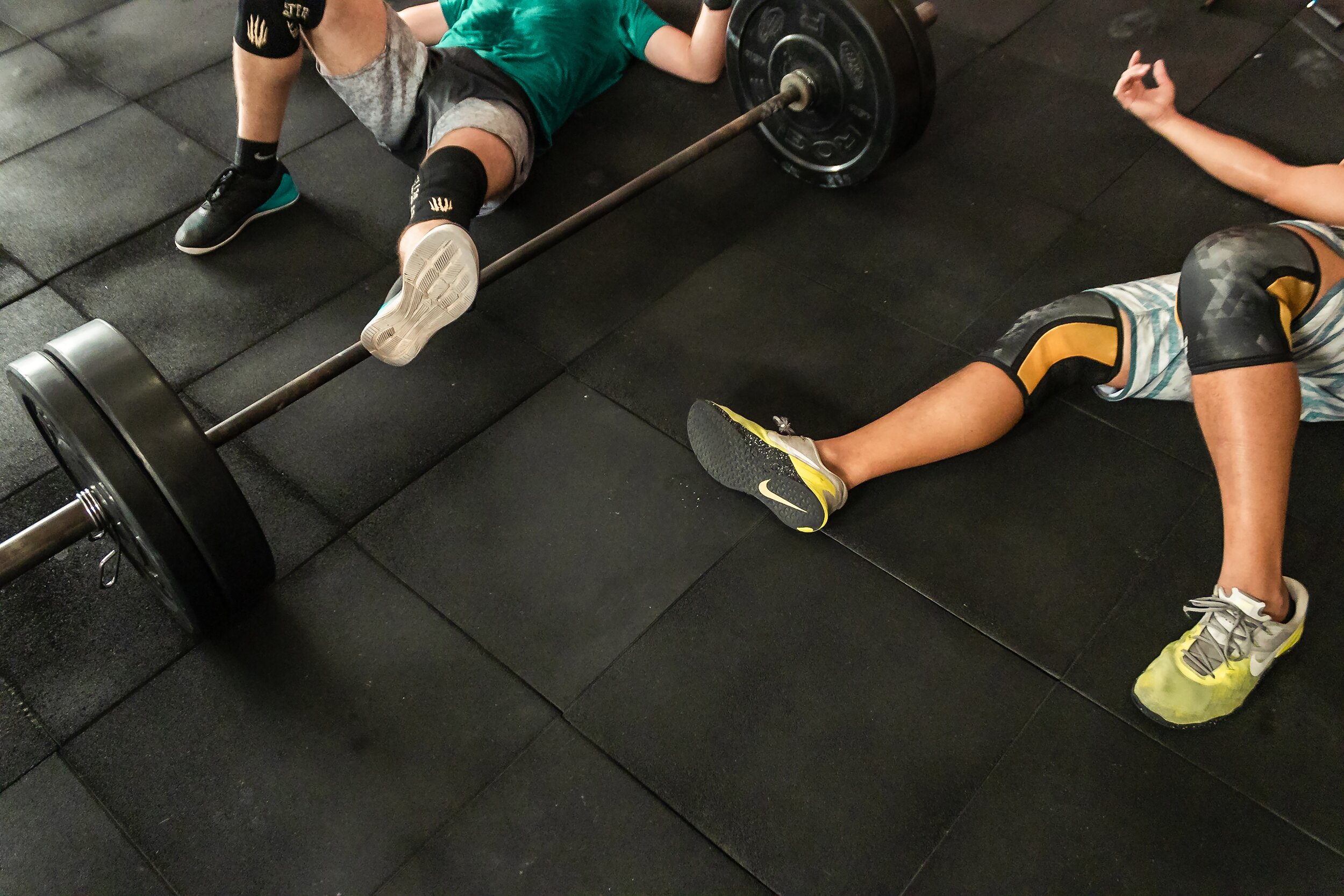two-men-lying-on-gym-floor-beside-black-barbell-2261483.jpg