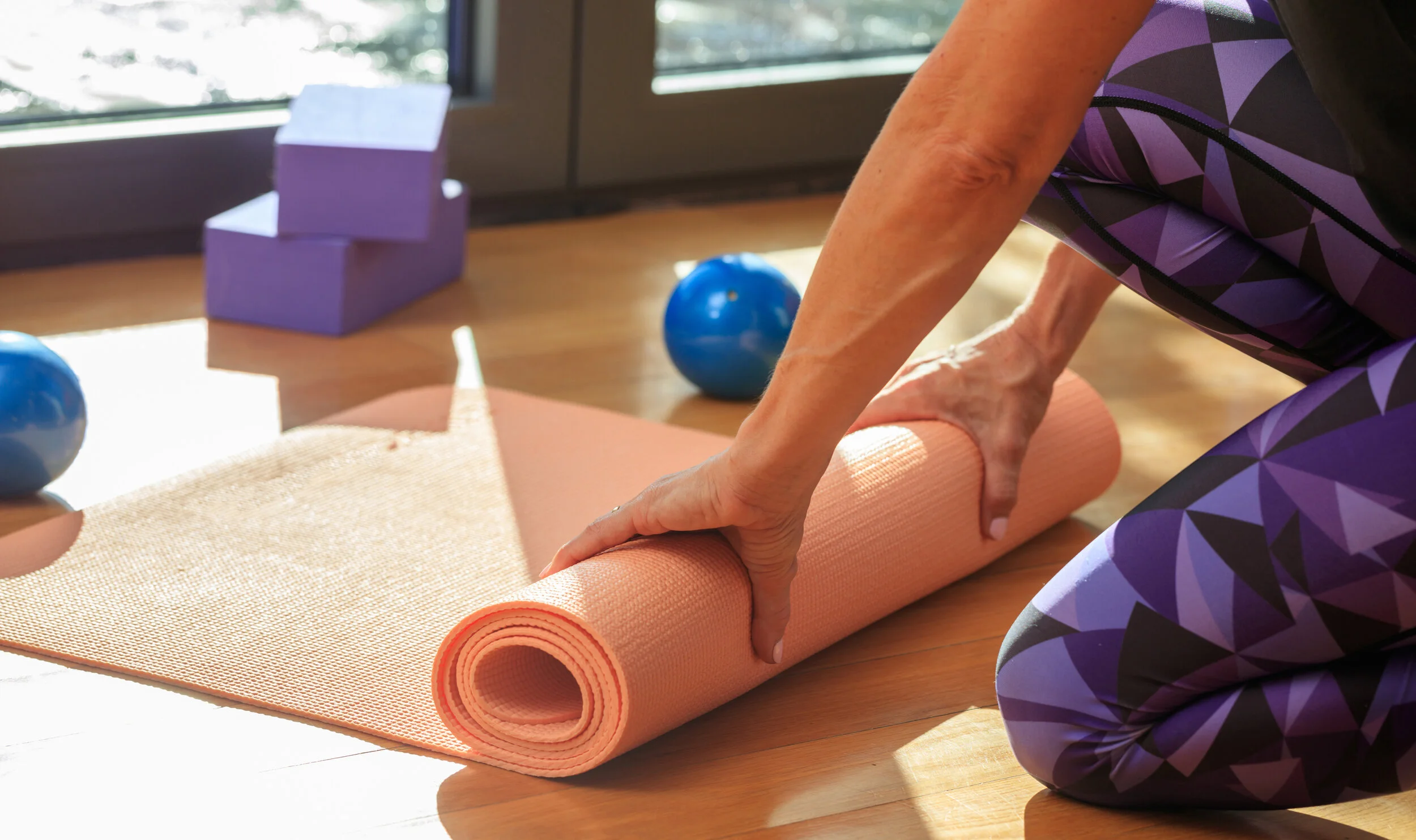 woman-rolling-a-yoga-mat-on-wooden-floor-P5Y8XZF.jpg