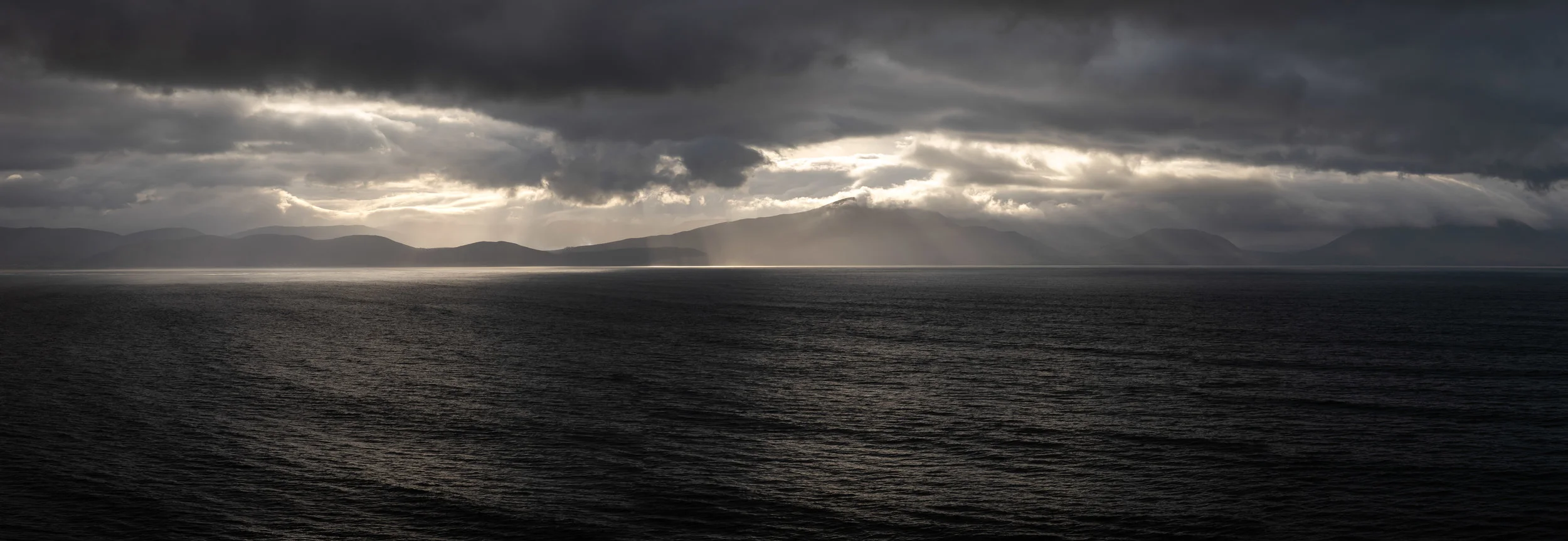 A pano image showing some fantastic god rays shooting out from the low cloud over the mountains