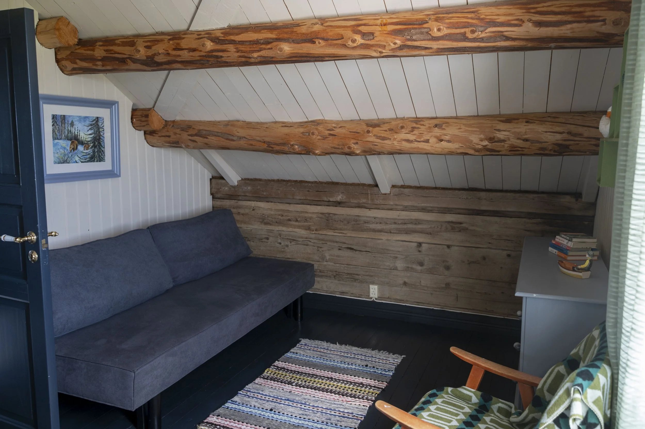 Et rom med tre store, naturfargede trestolper, en blå sofa og et fargesterkt stripete teppe på gulvet.