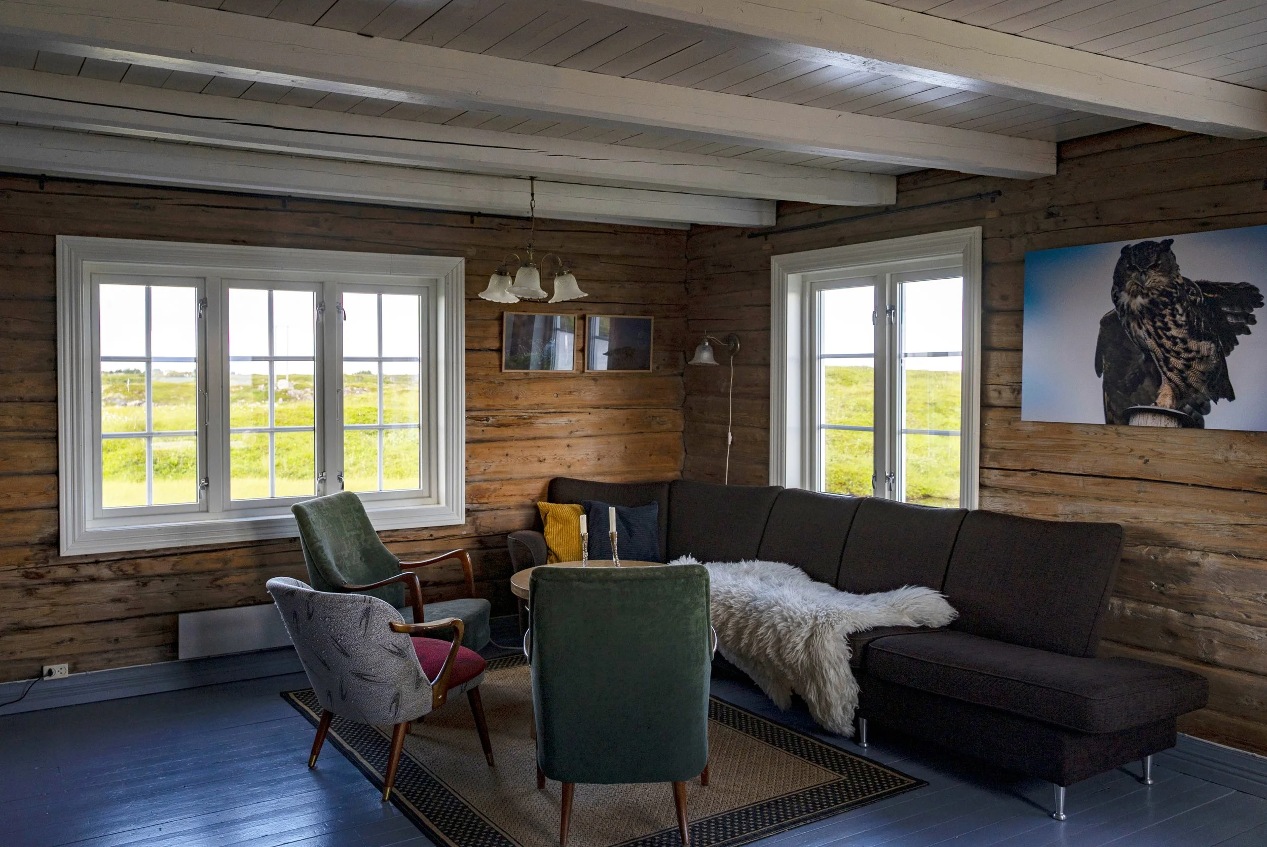Innendørs stue med tre store vinduer, tre puter i en sofa, en stol og et teppe på gulvet.